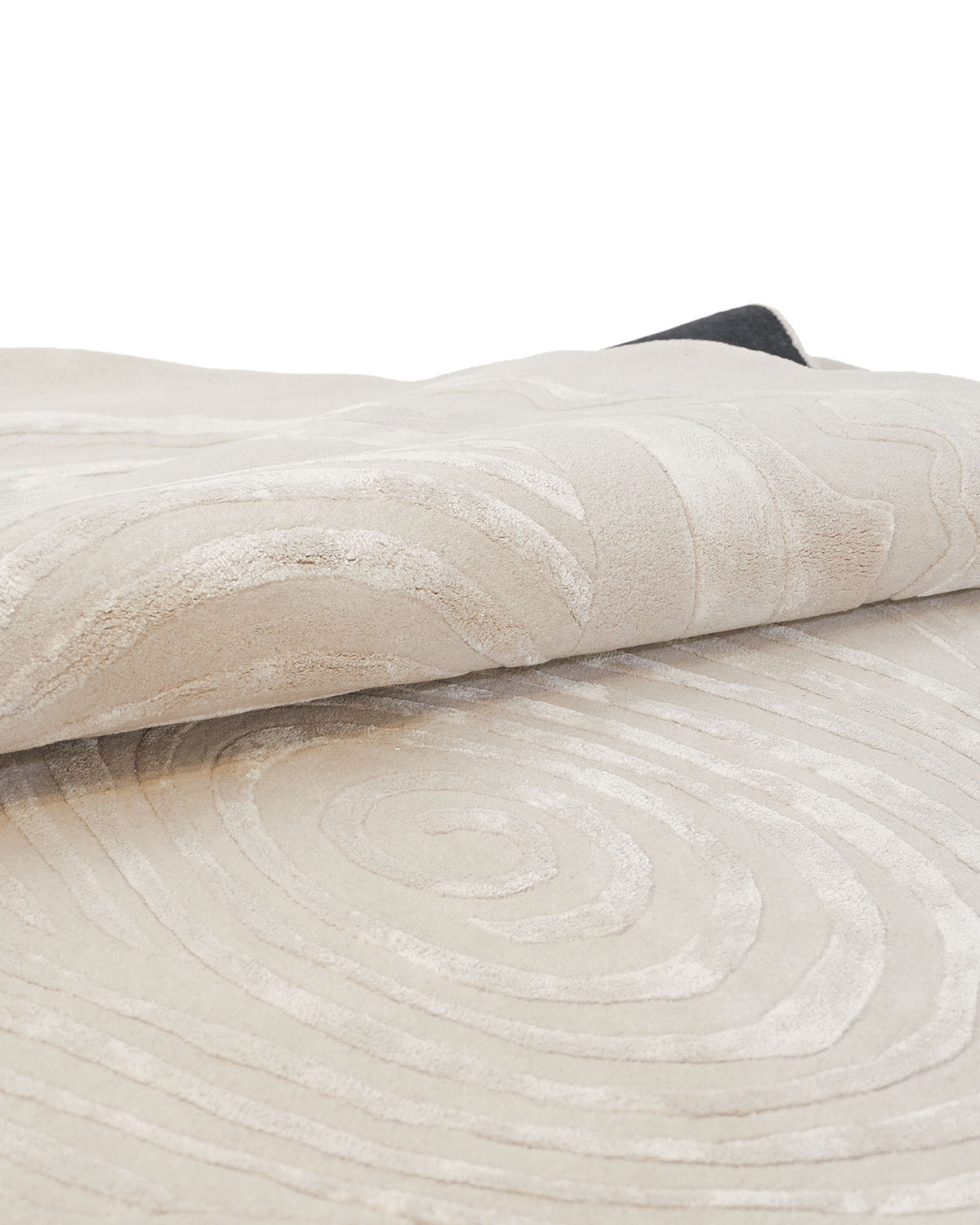 A close-up of the RAMSHA HOME “Abstract Beige Handcrafted Rug – Neutral Textured Modern Area Rug– HTWV 204” showcases its raised, swirling patterns, with a portion of the abstract rug folded to highlight its texture and thickness.