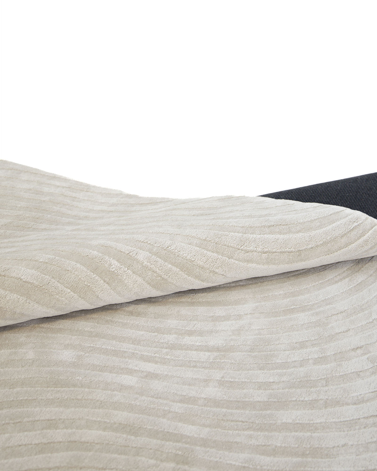 A close-up of the Off White Handmade Rug - HTV 14 by RAMSHA HOME showcases its beige, textured fabric with subtle horizontal stripes, partially folded over a dark surface—evoking inviting warmth and understated elegance.