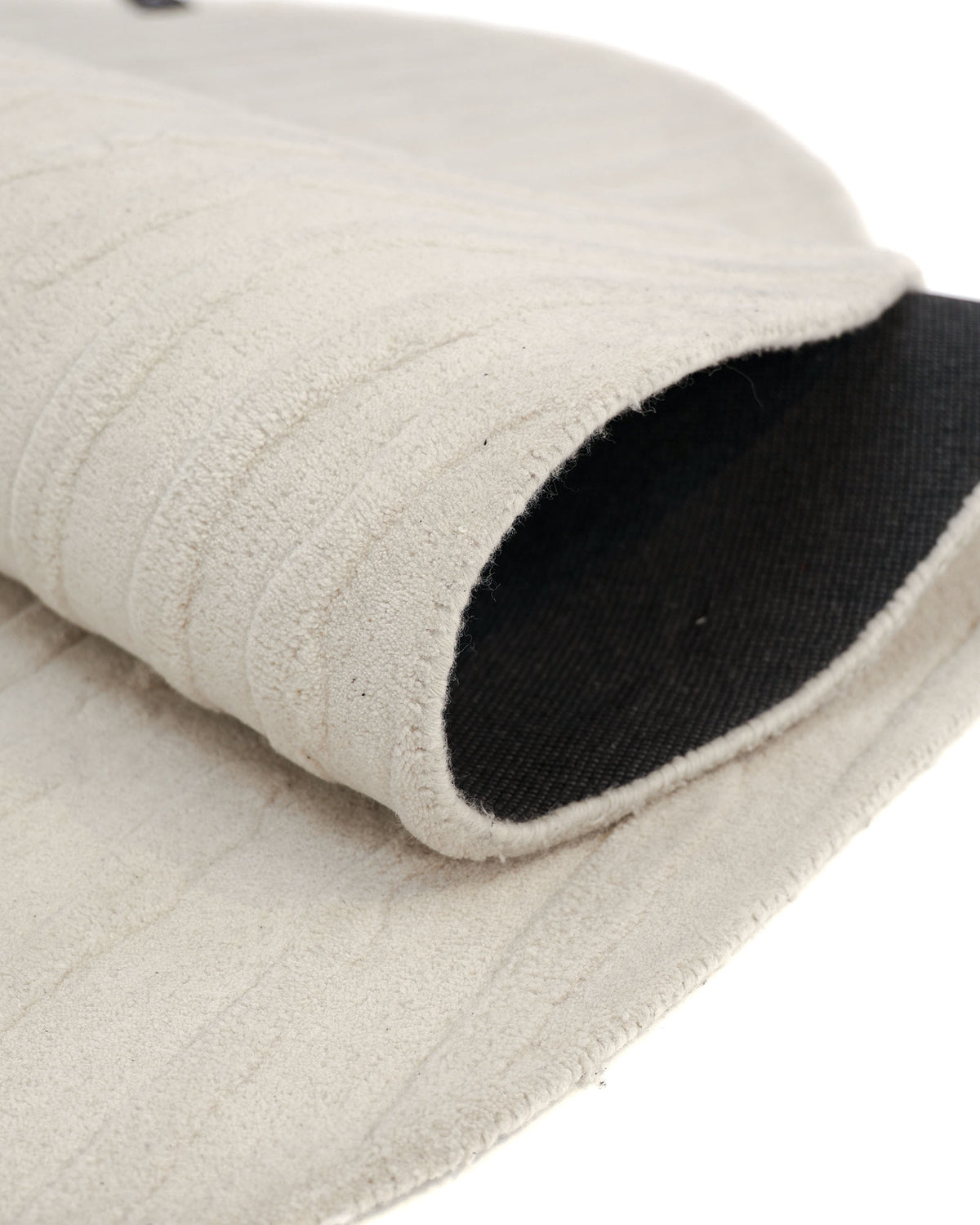 A close-up of the Irregular Shape Handmade Rug HTW 108 by RAMSHA HOME, featuring a rolled-up beige hand-tufted wool design with a textured surface and a dark underside, highlighting the edge and material layers.