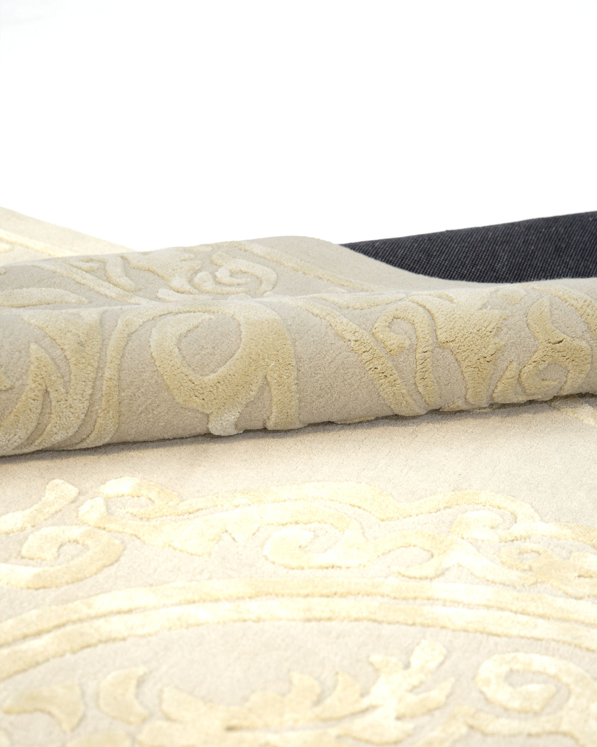 A close-up of the RAMSHA HOME Handmade Beige Area Rug 300x400 cm (HTWV-56), featuring an elegant gold and beige pattern with intricate medallion details, is shown partially folded to highlight its texture, while the dark backing is visible along the edge.