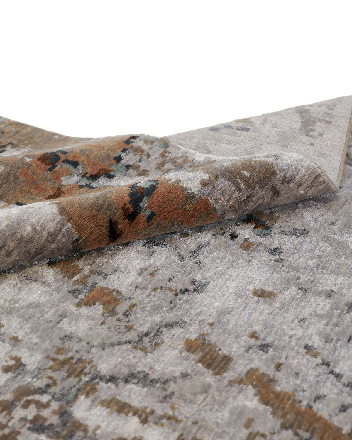 A close-up of the RAMSHA HOME Bamboo Silk & Cotton Hand Knotted Carpet HKWB-012, shown with a folded corner, displays an abstract pattern in shades of gray and brown with subtle touches of dark blue. This luxurious hand knotted rug seamlessly combines contemporary design and rich texture, making it a striking grey rust accent for any living area.