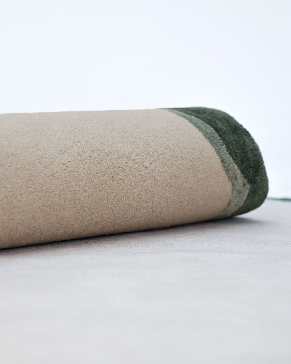 The Handmade Decorative Multi Color Rug HTWV-92 by RAMSHA HOME, featuring a rolled-up modern design with beige tones and a green edge, is displayed on a light-colored surface against a simple white background.