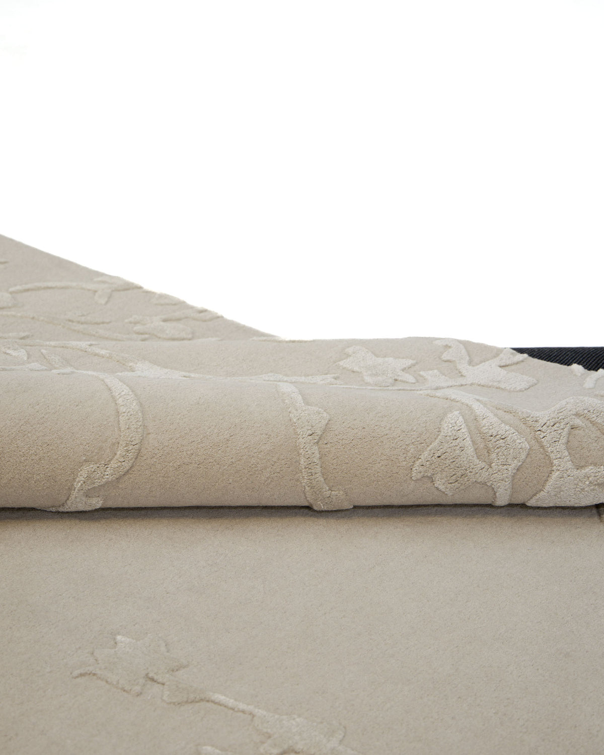 A close-up of the RAMSHA HOME Handmade Beige Color Decor Rug- HTWV 115, featuring raised abstract floral patterns in hand-tufted wool, partially rolled on a white background.