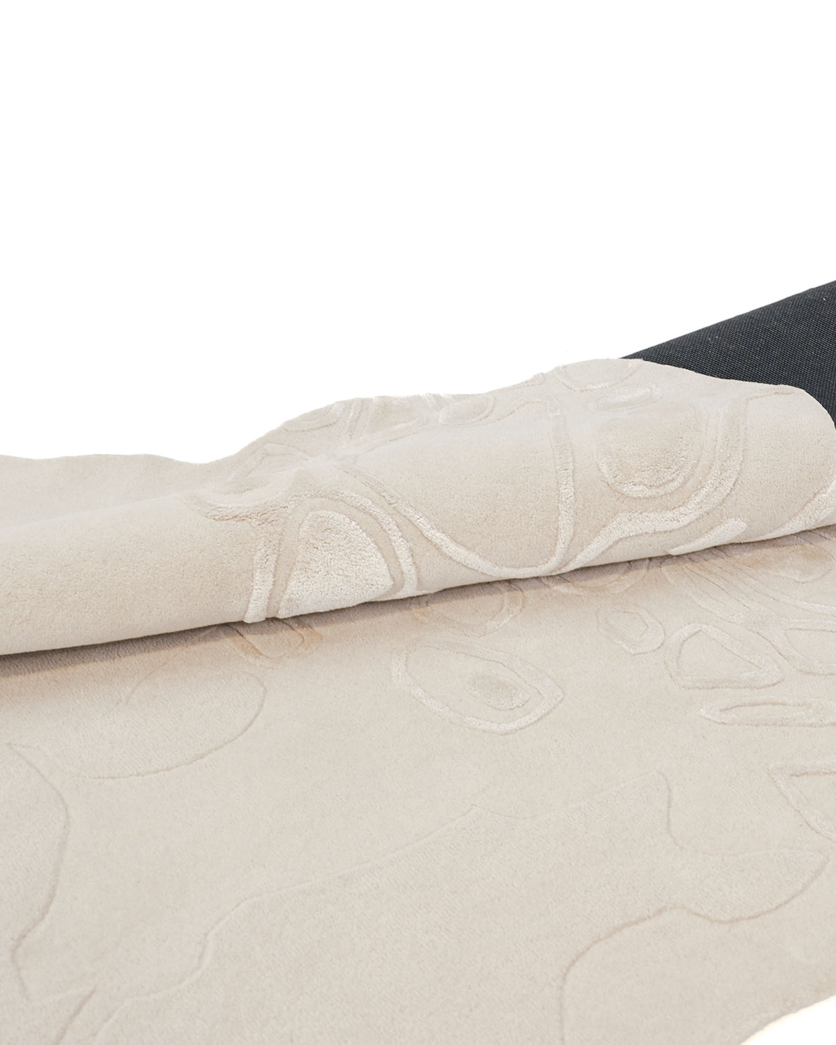 A close-up of the “Modern Sculptural Shape Rug Neutral Beige 200 cm – HTWV 207” by RAMSHA HOME showcases its light beige hue and textured, embossed shapes, with a partial fold revealing the striking black underside—ideal as a neutral centerpiece for modern interiors.