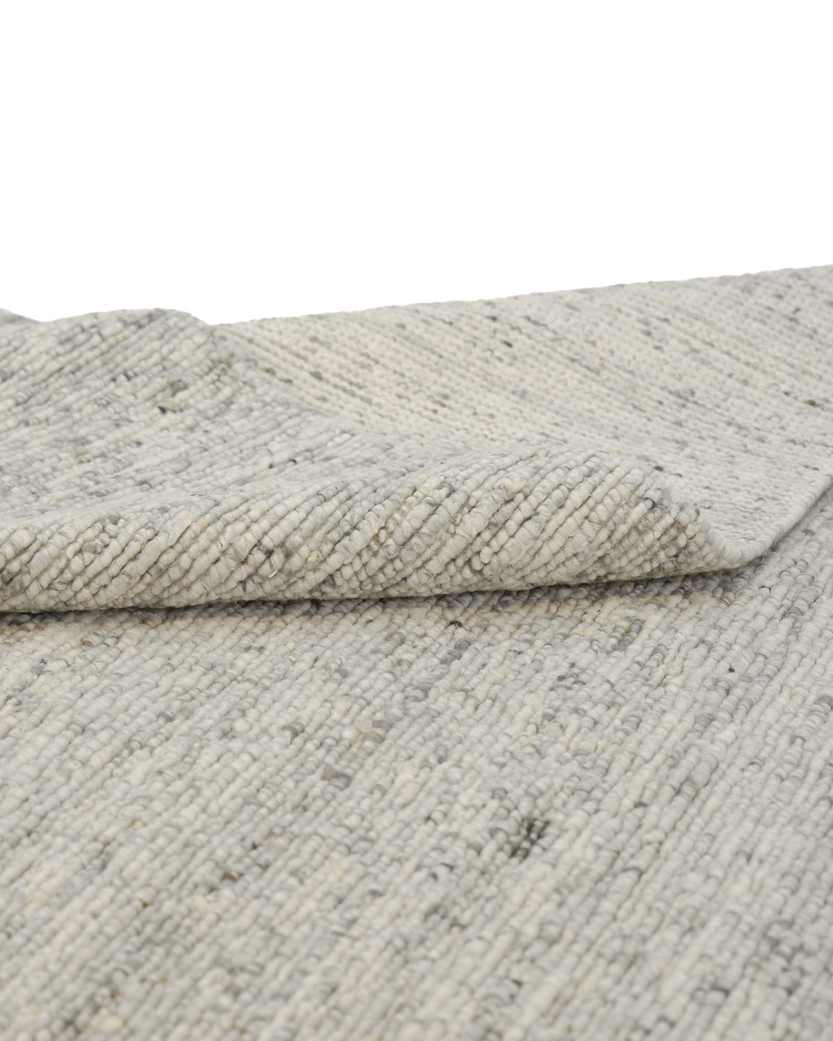A close-up of the Soft Terra Flatweave Wool Rug- SRN-043 by RAMSHA HOME reveals its textured, light gray woven surface with subtle specks, featuring one corner slightly folded to showcase the underside. This handmade rug exemplifies traditional craftsmanship and stands as an ideal neutral color piece, adding understated elegance to any room.