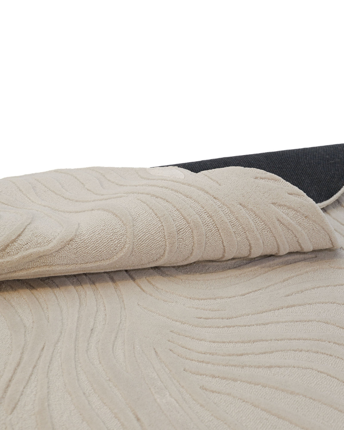 A close-up of the RAMSHA HOME Organic Shape Flow Line Handmade Area Rug HTWV-141 shows its irregular beige surface with curved, raised patterns and a corner folded over to reveal a dark non-slip backing underneath.