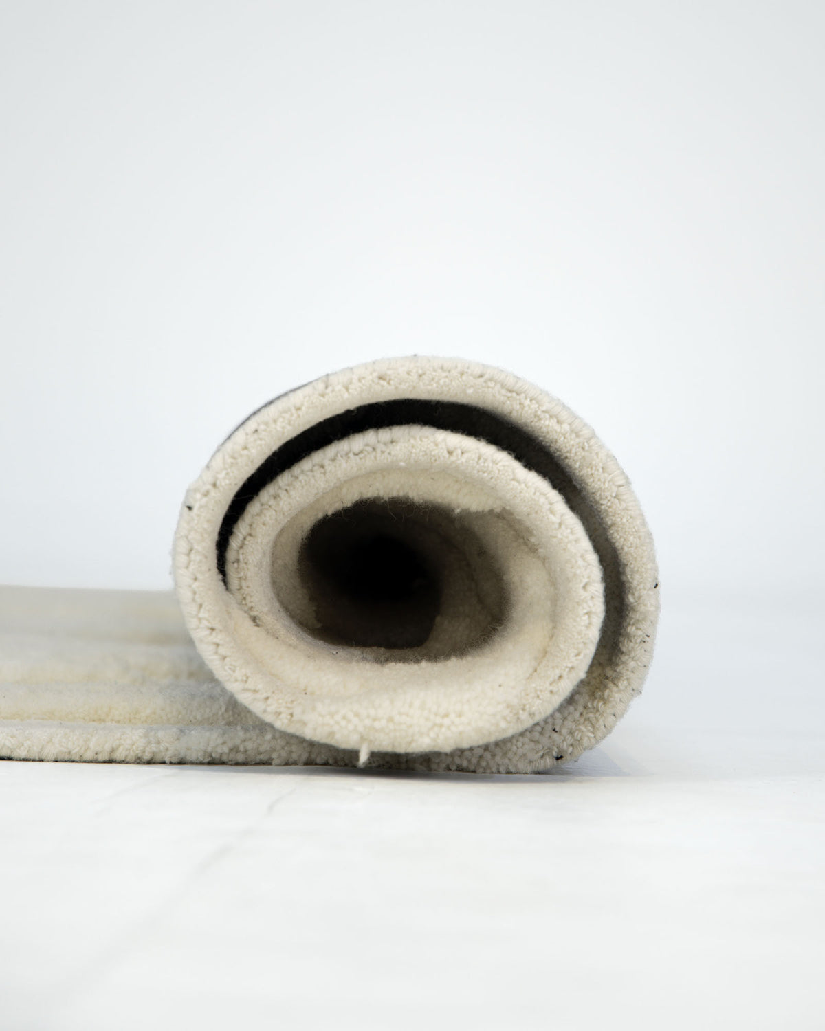 The RAMSHA HOME Beige Color Oval Shaped Handmade Rug - HTWV 106 (200x300cm) is partially rolled up with the spiral end facing the camera, set against a plain white background.