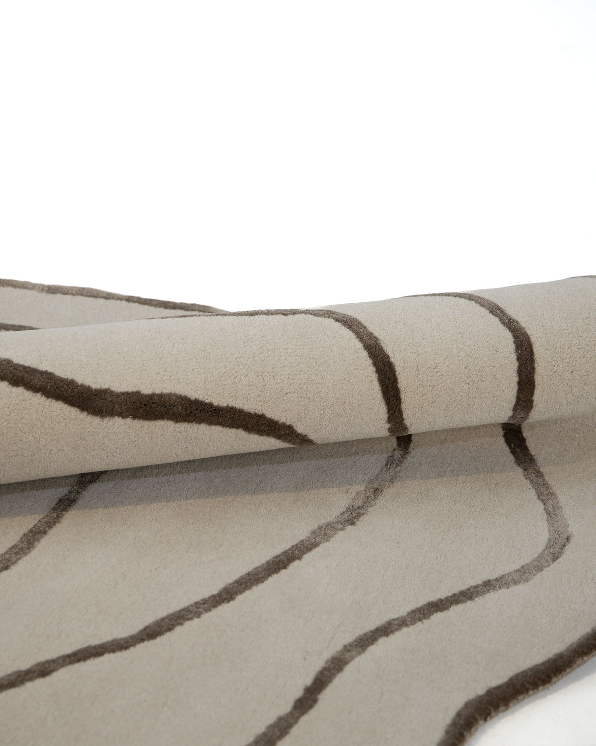 The RAMSHA HOME Handmade Multi Color Hand-Tufted Area Rug HTWV-65, featuring irregular wavy brown lines on a beige background, is shown partially rolled on a white surface.