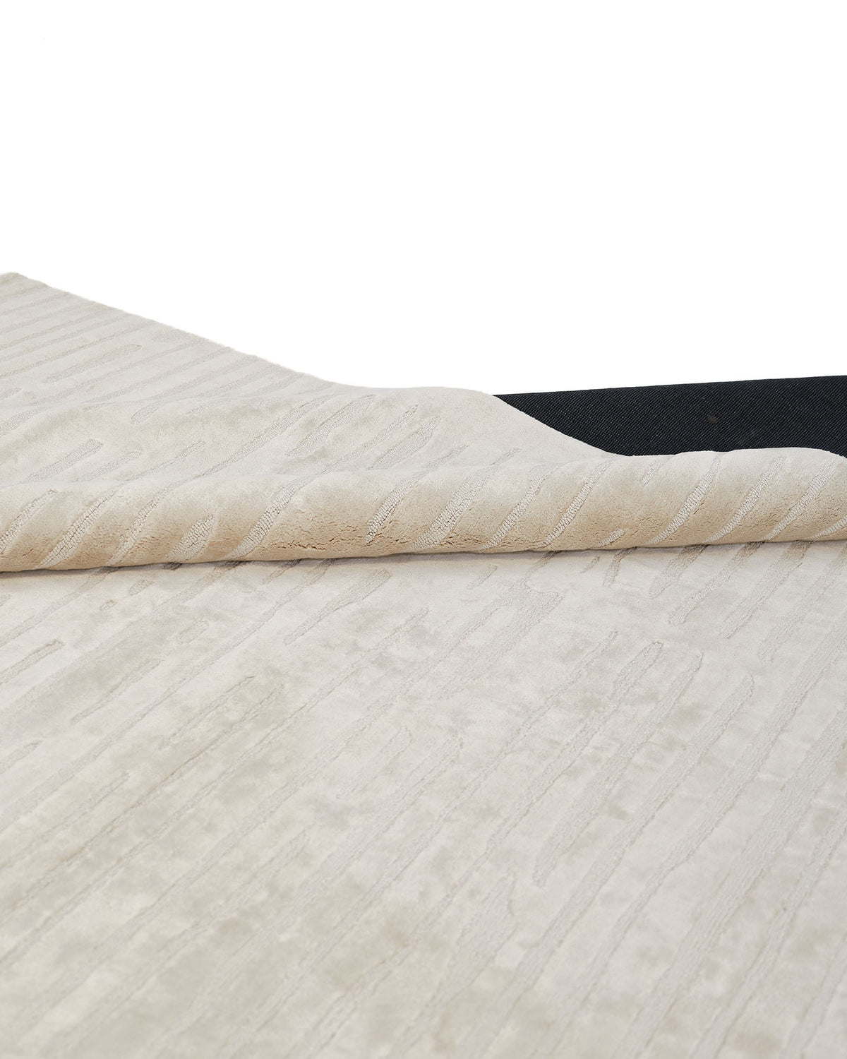 A close-up of the corner of the RAMSHA HOME Home Decor Handmade Area Rug - HTV 17 in a neutral texture being lifted to reveal a black rug pad underneath, set against a white background.