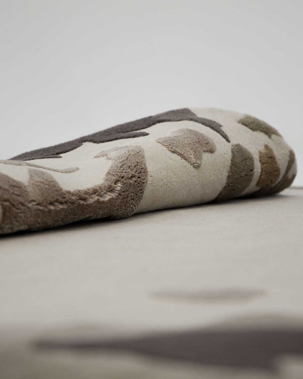 A close-up of the RAMSHA HOME Terra Eclipse Oval Handmade Rug Accent Rug HTWV-195, featuring a rolled beige and brown camouflage-inspired pattern—ideal as a modern accent piece for your interior—displayed on a plain surface with a neutral background.