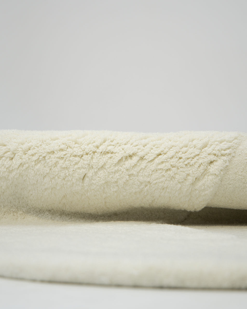 Close-up view of the Handmade Shape White Color Area Rug - HTW 101 B by RAMSHA HOME, featuring soft, cream-colored, fluffy wool with a textured, plush surface—perfect as an irregular hand-tufted area rug—shown against a plain light background.