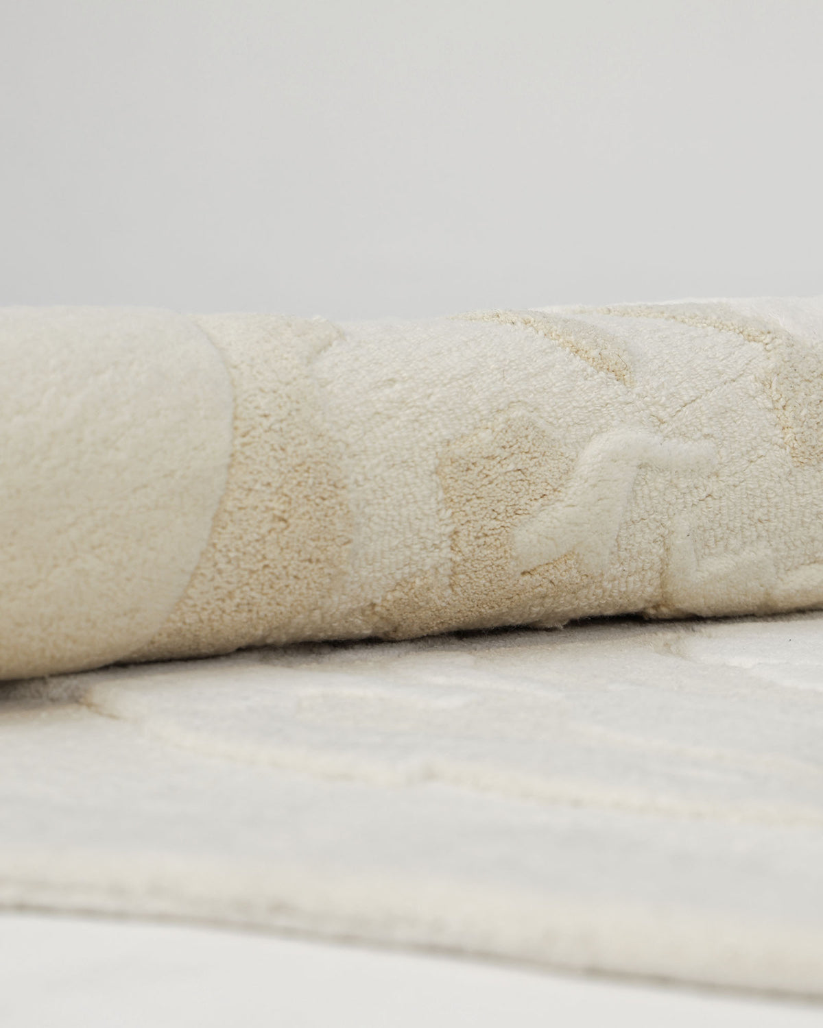 A close-up of the RAMSHA HOME Stylish Handmade Shape Rug Multi Color HTWV-105 showcases its neutral light beige tones and subtle textured pattern, rolled neatly on a flat surface with a simple, plain background.