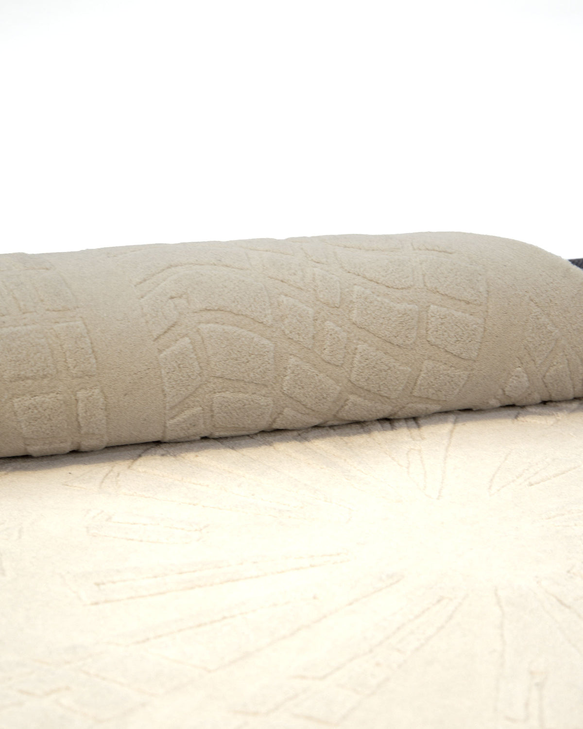 A close-up of the RAMSHA HOME Rectangle Shape Beige Color Handmade Area Rug - HTW 132 (200x300 cm), partially rolled up, highlights its geometric embossed pattern across both the rolled and flat sections.