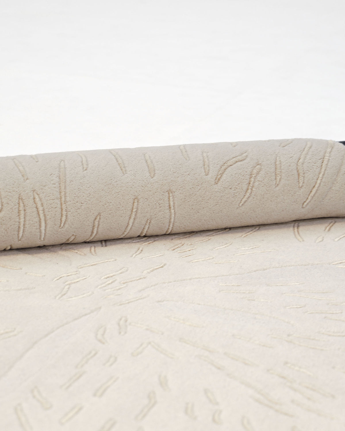 A close-up of a rolled-up, light grey Embossed Floral Solid Rug – HTWV 171 by RAMSHA HOME, featuring subtle, wavy, raised line patterns on its hand-tufted surface, set against a plain white background.