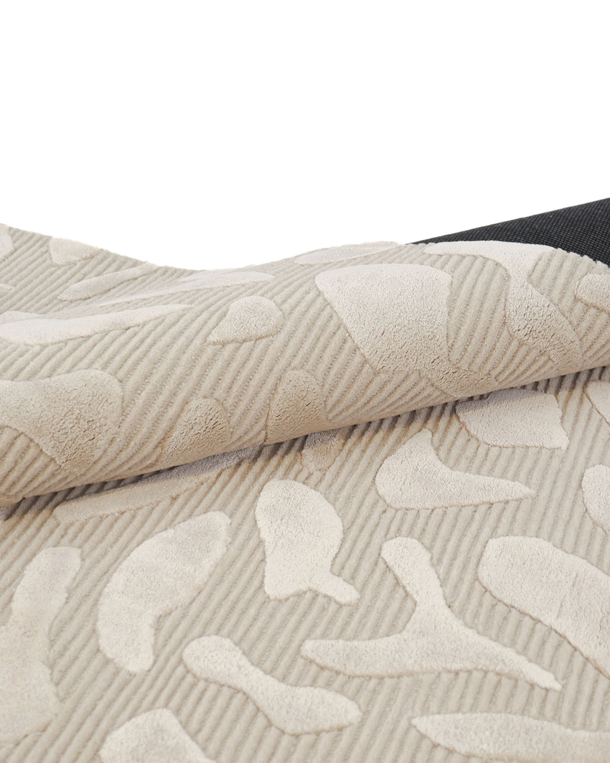 Close-up of the RAMSHA HOME Modern Beige Textured Rug – Abstract Organic Pattern Neutral Area Rug (HTWV 203), featuring raised, abstract shapes and a ribbed texture. The neutral rug is shown partially folded to reveal its black underside along the top edge.