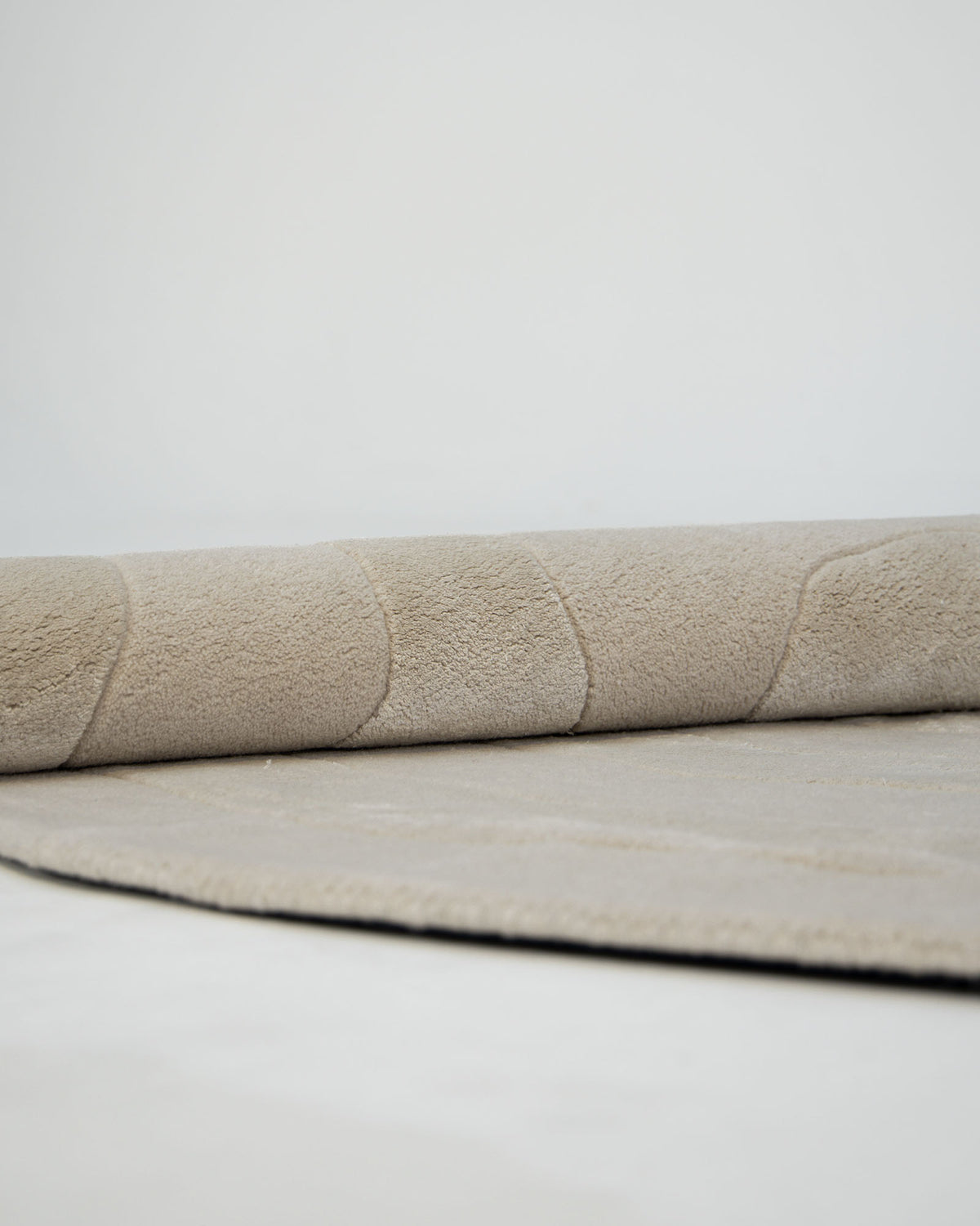 A close-up of the RAMSHA HOME Wool & Tencel Multi Color Rug HTWV-91, featuring a light beige hand-tufted design, partially rolled up on a white floor against a simple, minimalistic background.
