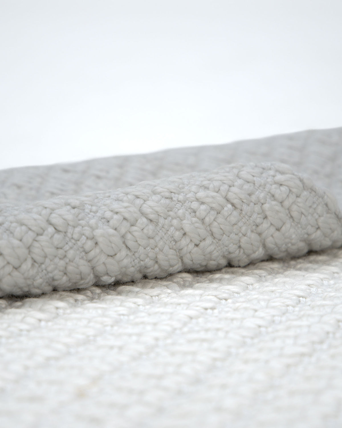 Close-up of the Handmade Cream Natural Color Hand Woven Area Rug WR-039 by RAMSHA HOME, showcasing its folded, textured surface and chunky knit pattern in a soft, neutral hue—the perfect artisanal accent for elevating any space.