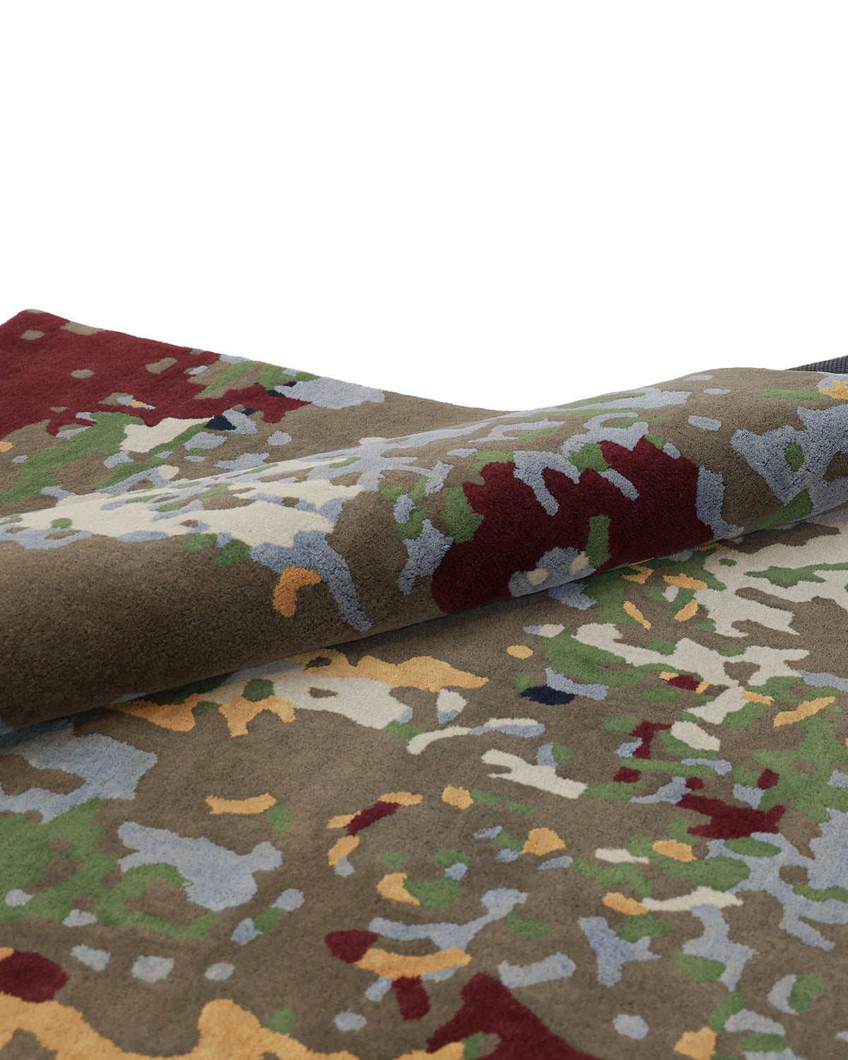 A close-up of the RAMSHA HOME Modern Artistic Handmade Rug 240x300 cm (ZUA-21) highlights its folded edge and abstract pattern, showcasing earthy shades of brown, green, red, and yellow—an ideal choice for infusing any space with artistic flair.