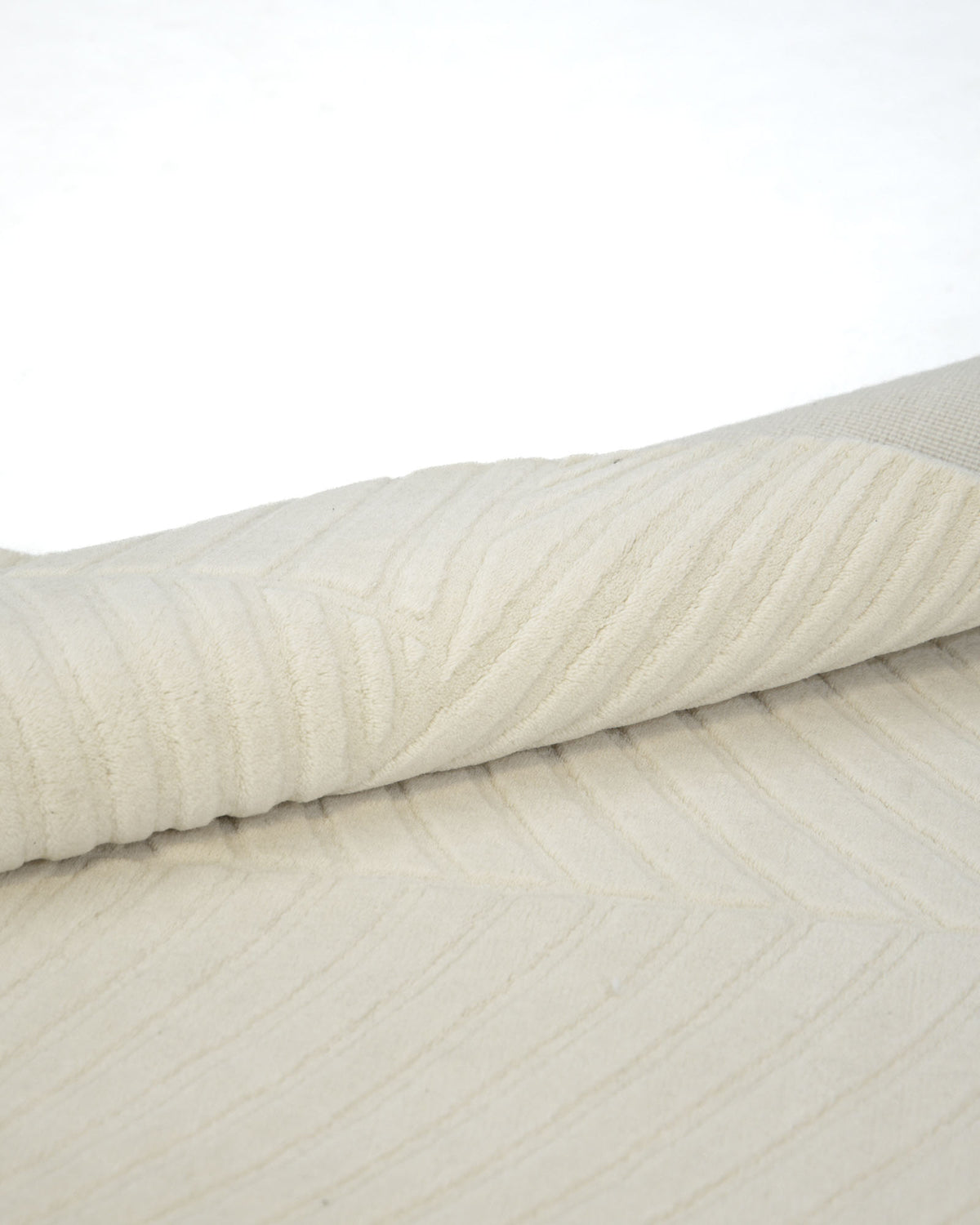 A close-up of the RAMSHA HOME Natural Color Handmade Area Rug - LKH-018 (200x300 cm), featuring a cream-toned, loom knotted wool construction with a subtle geometric pattern, partially rolled over itself on a white surface.