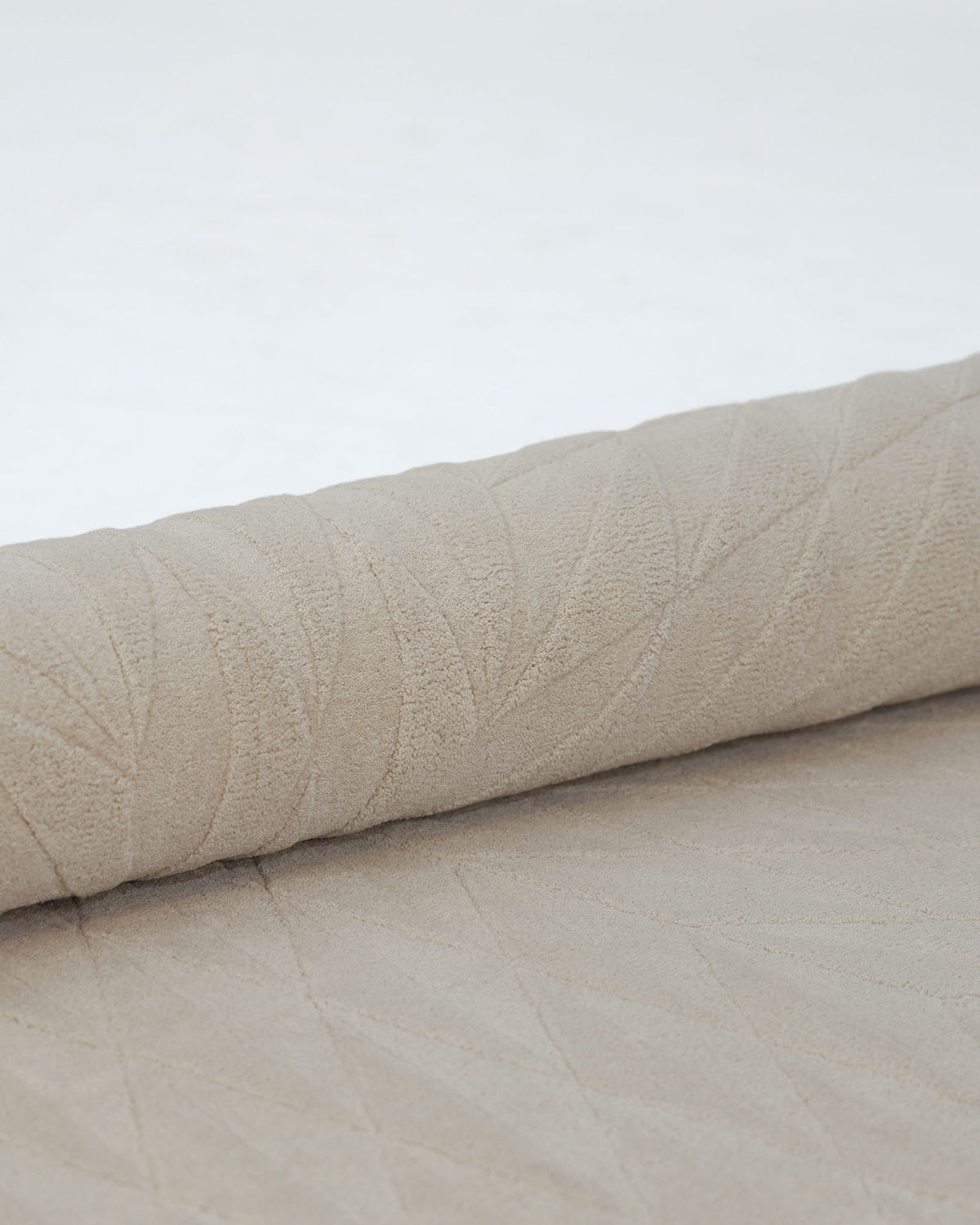 A close-up of the RAMSHA HOME Beige Handmade Round Rug HTW 107 (200cm), partially unrolled on a white surface, highlights its artisanal craftsmanship and subtle leaf-patterned texture, evoking the natural beauty of handcrafted fiber rugs.