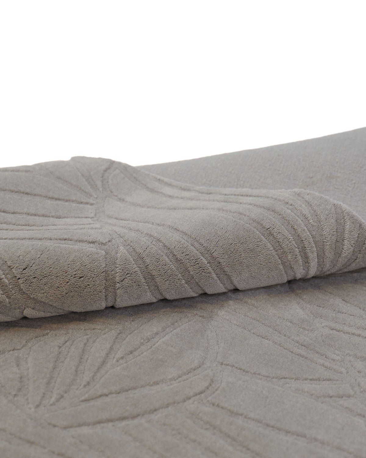Close-up of the Rectangle Handmade Decorative Grey Color Area Rug - LKH-030 by RAMSHA HOME, featuring a folded section with a raised, textured geometric or abstract leaf pattern on its surface, reminiscent of the intricate detailing often found in loom-knotted wool rugs.