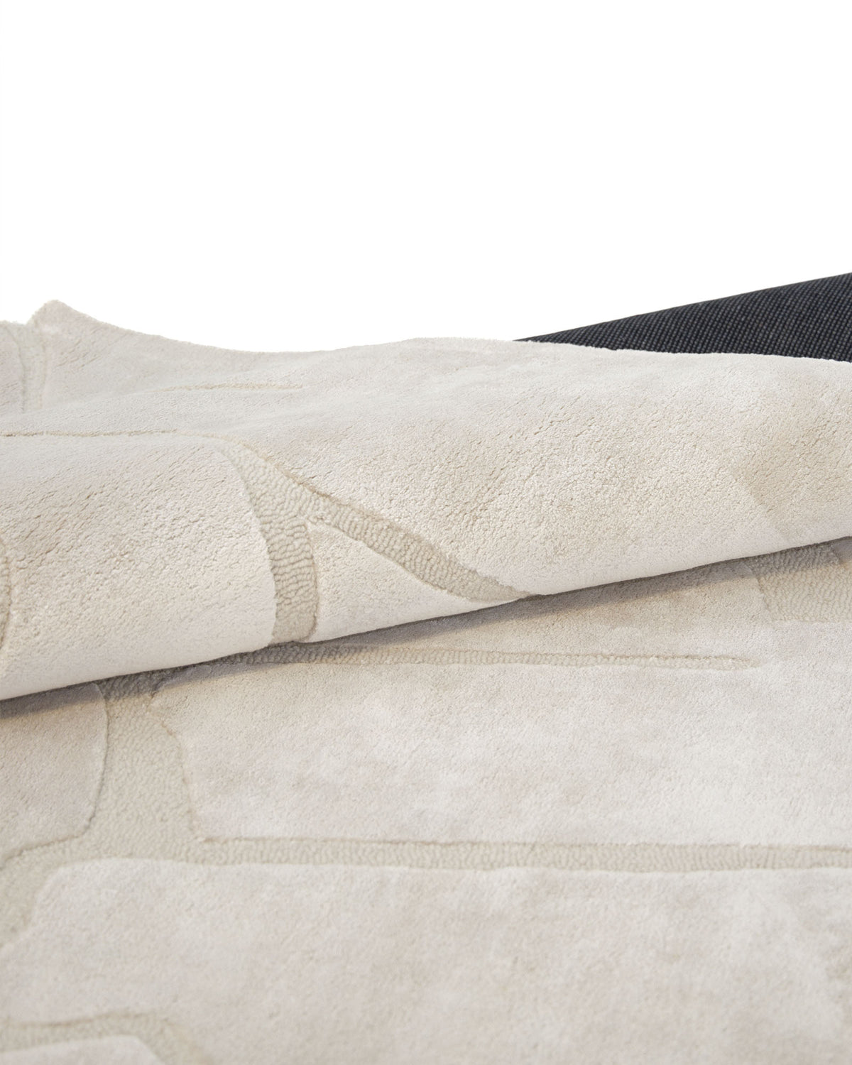 A close-up of the RAMSHA HOME Modern Viscose & Wool Handmade Carpet 200x300 – HTWV-172 showcases its subtle geometric pattern in beige tones, with the rug partially folded to reveal the textured black backing underneath.
