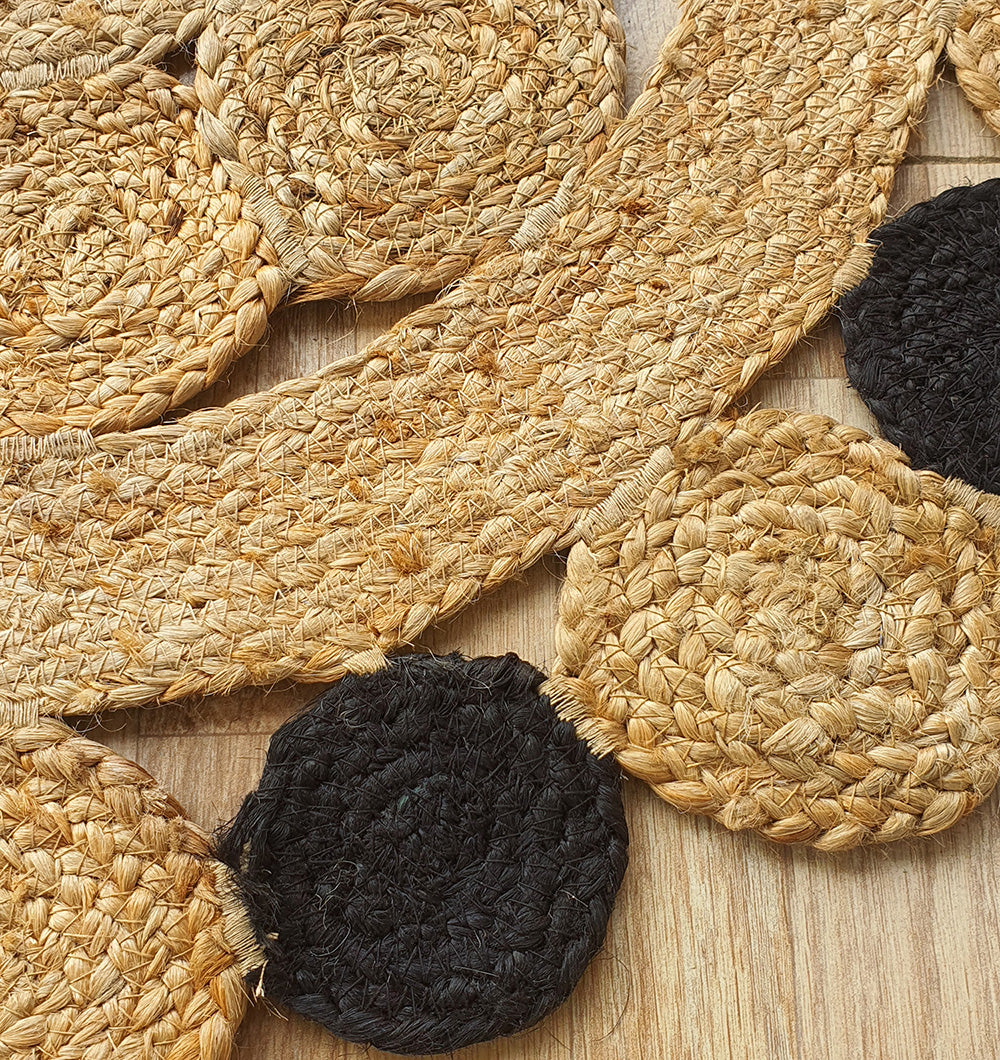Close-up of RAMSHA HOME’s Oval Shaped Jute Braided Rug Black & Natural BR-033 arranged on wood, displaying its natural fiber texture and contrasting tan and black design.