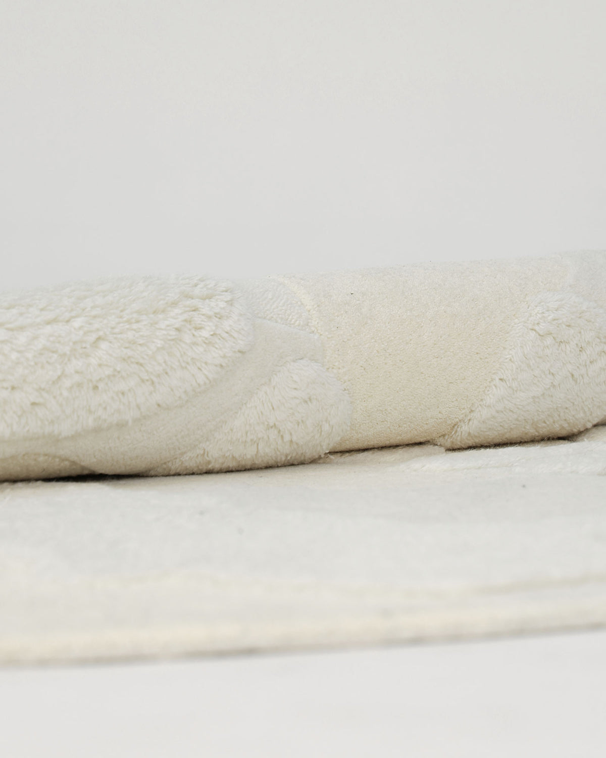 A close-up of the Creative Multi Color Wool & Cotton Handmade Rug - HTW 69 (200x300cm) by RAMSHA HOME, showcasing its soft, plush texture as it lies gracefully on a flat surface against a plain white background—evoking an air of subtle elegance and cozy appeal that defines hand-tufted wool rugs.