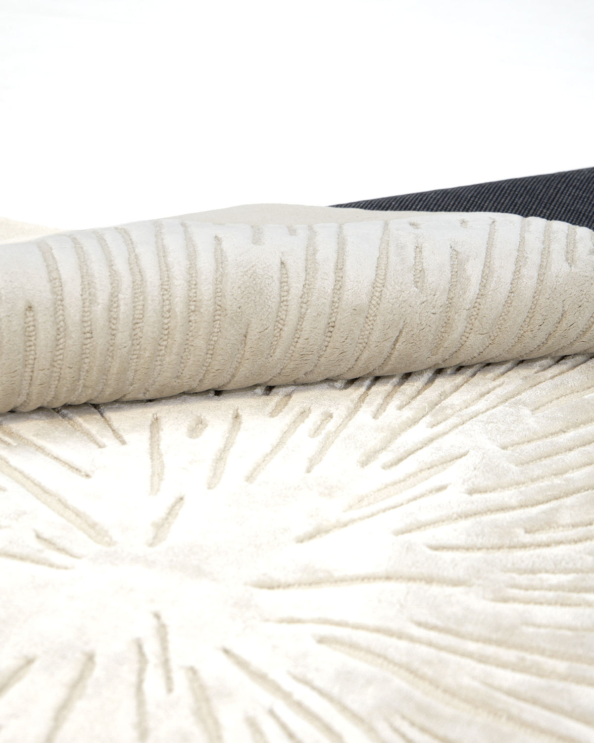 The RAMSHA HOME Hand-Tufted Carpet For Home Decor HTWV-76 features a light beige, contemporary design with a raised sunburst pattern and is partially rolled to reveal its dark backing. Its rich texture and striking pattern add depth and softness, making this rug a perfect neutral floor covering for modern interiors.