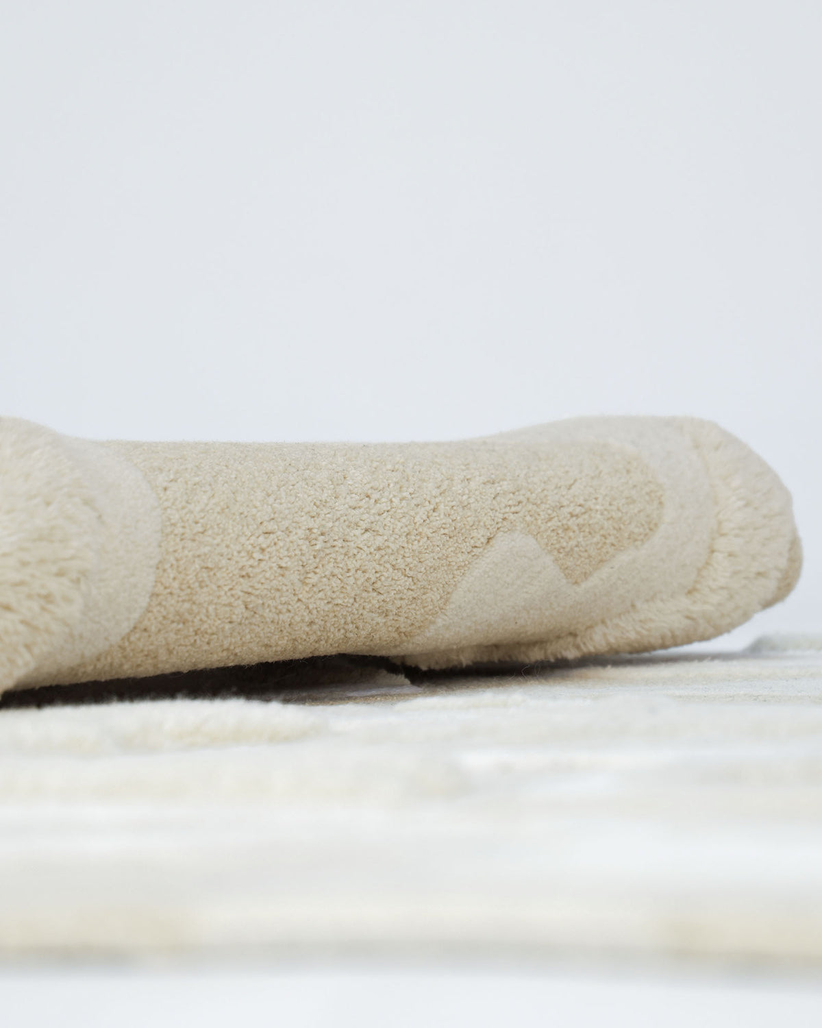 A close-up of the Handcrafted Natural White Area Rug – HTWV-129 by RAMSHA HOME, rolled up on a matching surface. The soft, inviting texture and subtle color palette evoke the comfort and warmth of this handtufted piece, making it an ideal addition to a modern setting with minimal background distraction.