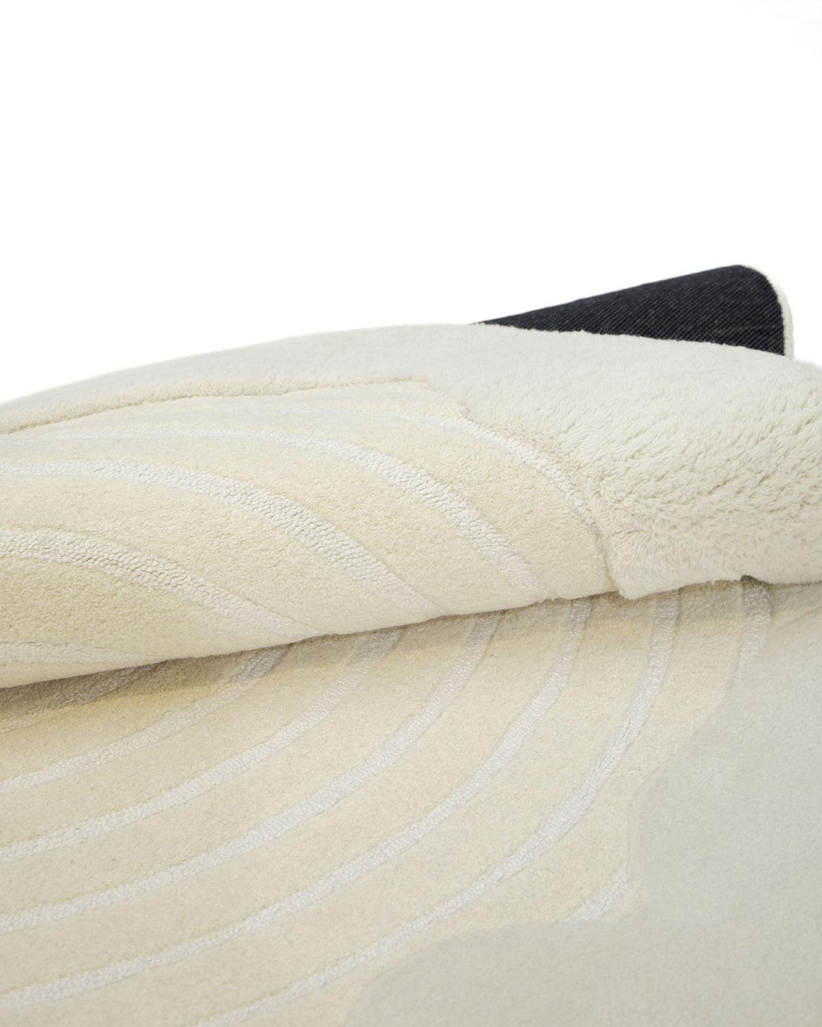 Here is a rewritten sentence using the provided product and brand information: A close-up of the RAMSHA HOME Natural White Color Handmade Area Rug - HTWV-138 (183 x 200 cm) reveals its refined hand tufted craftsmanship, with subtle curved patterns in a soft beige hue. The partially folded rug displays its plush underside and contrasting dark backing, bringing warmth and elegant texture to any space.
