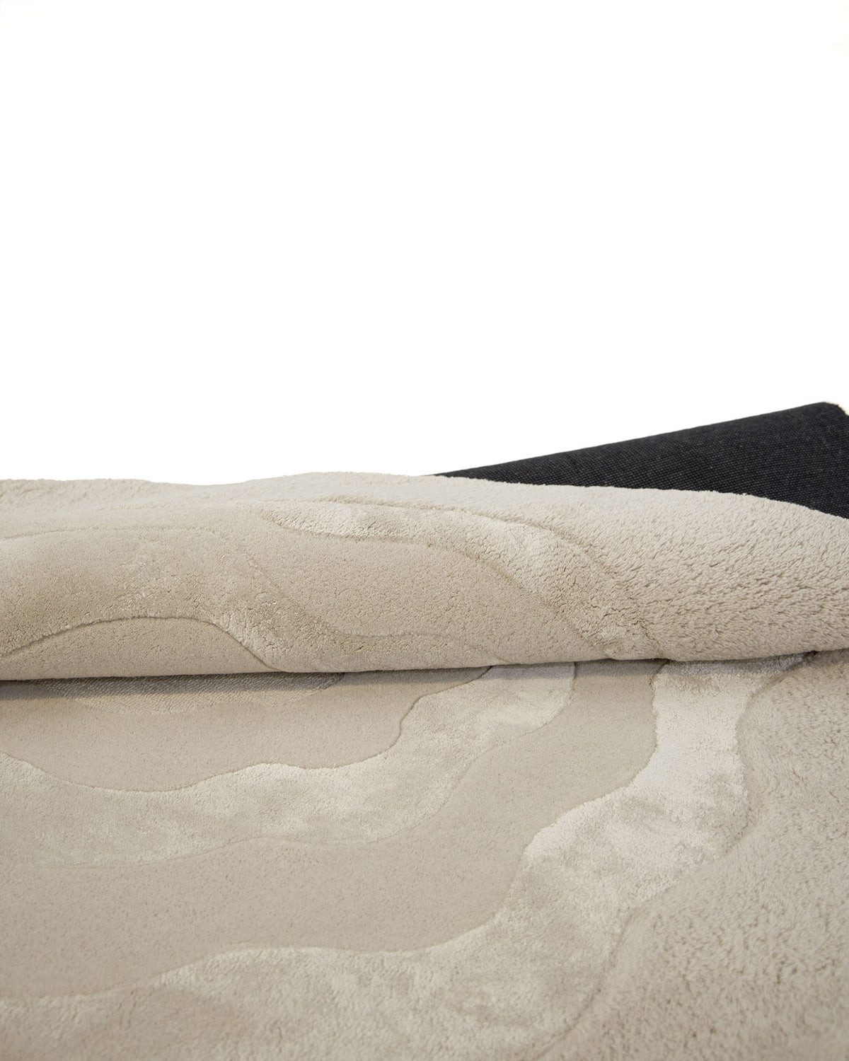 A close-up of the Multi Color Handmade Area Rug - HTWV 148 by RAMSHA HOME showcases its hand-tufted wool blend composition with wavy patterns, partially rolled to reveal a dark backing against a white background. This neutral area rug features an elegant texture that adds warmth and sophistication to any space.
