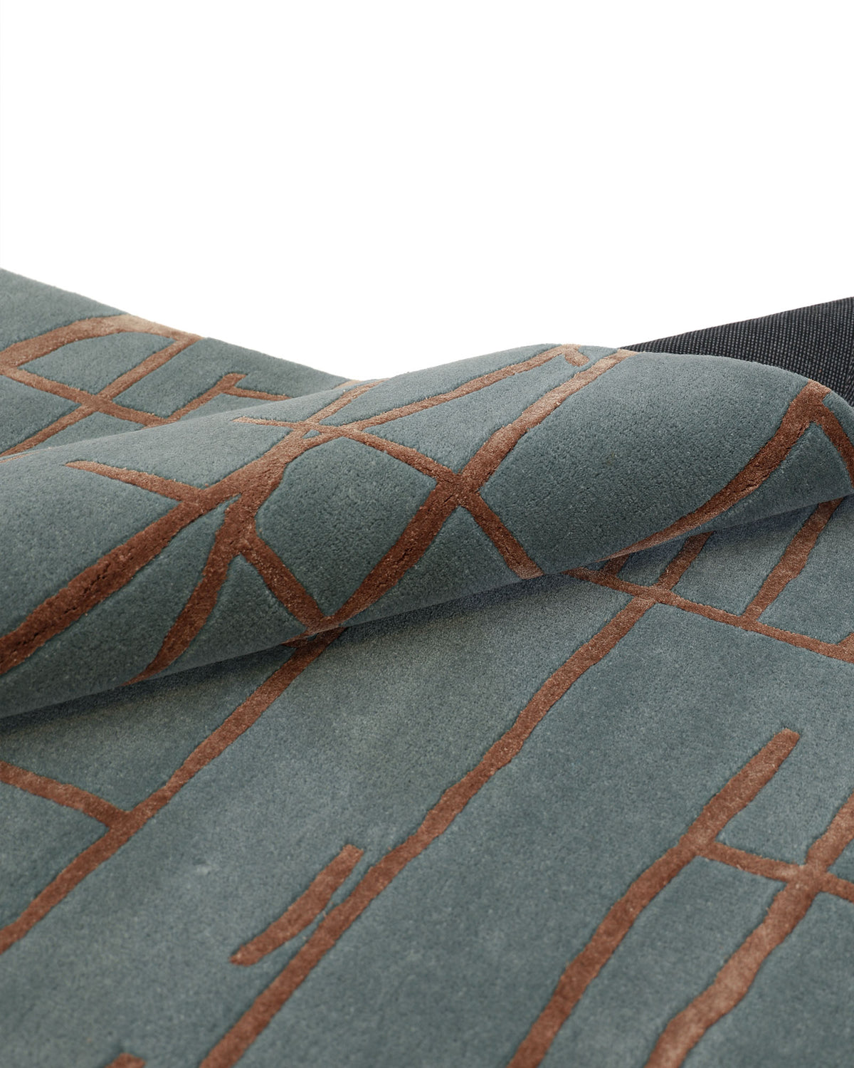 A close-up of the RAMSHA HOME Abstract Rust Line Grid Teal Rug – HTWV-31 (180x270 CM) highlights its hand-tufted texture in gray, featuring thin, irregular rust-brown lines forming a branching grid pattern. The edge of this premium wool-viscose rug is slightly lifted, showcasing its plush thickness and subtle texture.