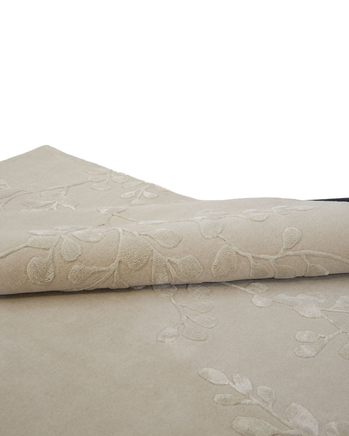 A close-up view of the RAMSHA HOME Artisan Handmade Decorative Area Rug – HTWV-116 in beige highlights its hand-tufted texture and subtle raised leaf pattern. The botanical area rug is partially rolled, showcasing its intricate design and craftsmanship.