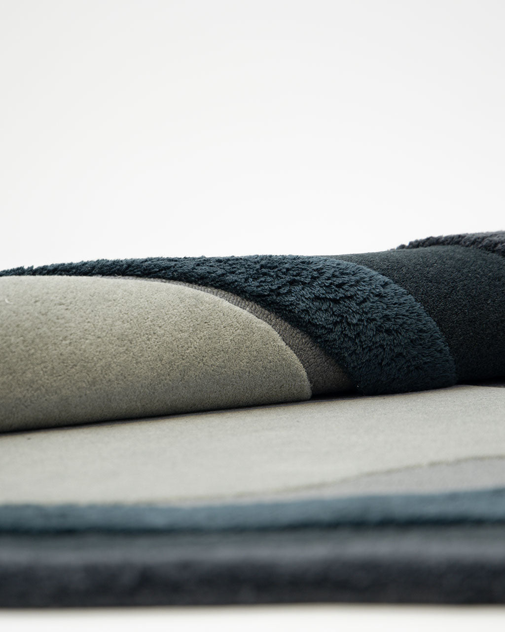 A close-up of the Handmade Layered Abstract Shaped Rug HTW 131 by RAMSHA HOME (200 x 300 cm) showcases its plush and smooth fabric layers in dark green, gray, and textured black sections—evoking a sophisticated blend of textures reminiscent of luxurious modern textiles—set against a plain background.