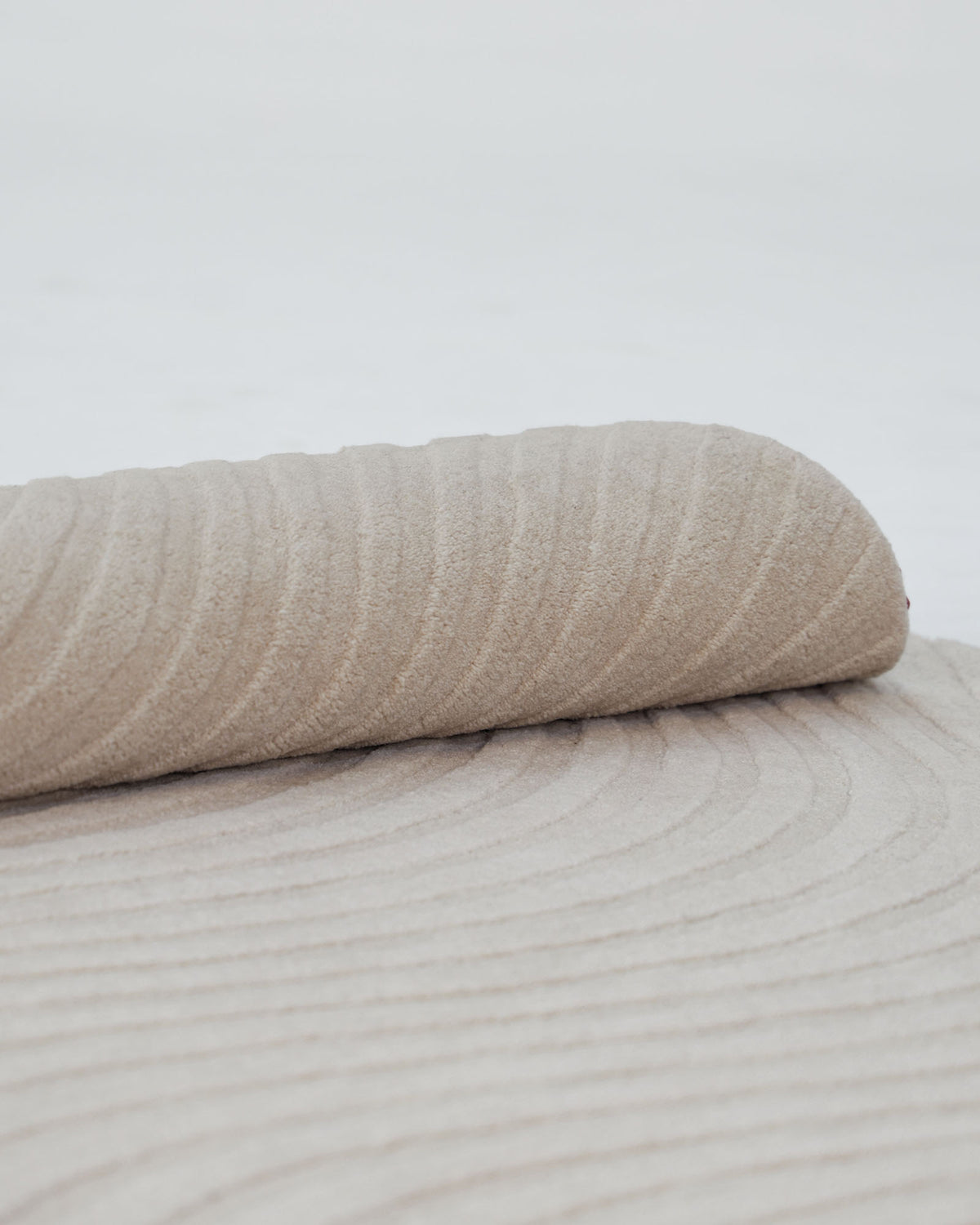 A close-up of the Home Decor Handmade Area Rug - HTW 96 by RAMSHA HOME, featuring a rolled beige wool design with subtle, wavy textured patterns on its surface, set against a light background.