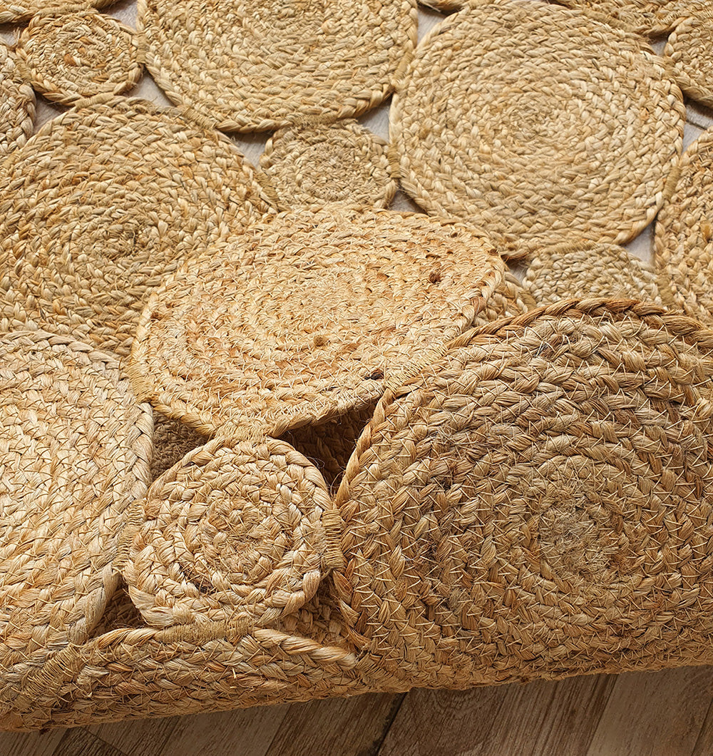 Close-up of RAMSHA HOME’s Handmade Circular Pattern Jute Rug BR-035, shown with other woven mats in overlapping circles on a wooden floor. The rugs feature textured jute for a natural, rustic look and come in varied sizes.