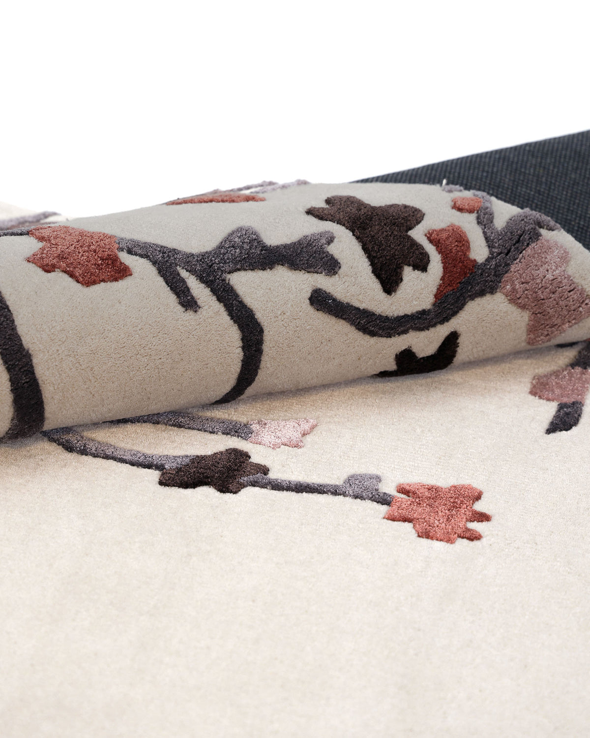 A close-up of the RAMSHA HOME Multi Color Handmade Area Rug HTWV-119 in beige, featuring an intricate black, brown, and pink floral pattern. Partially rolled to highlight its luxurious texture and finely crafted underside, this decorative area rug adds elegance to any space.