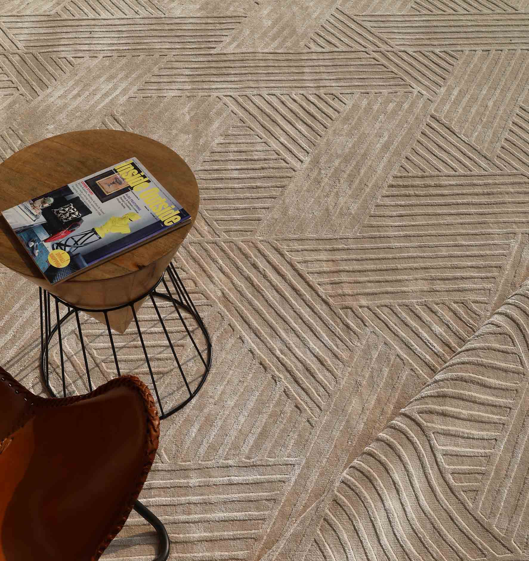 A round wooden side table with black metal legs holds a magazine and sits beside a brown leather chair on the RAMSHA HOME Textured Geometric Home Decor Handmade Area Rug - LKH-06.