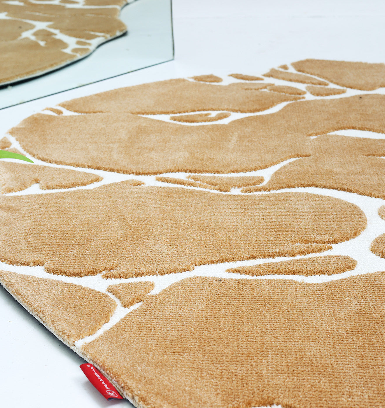 Close-up of the Novara Shape Rug Multi Color CMN-13 by RAMSHA HOME, featuring an organic tan and white abstract pattern. Reflected in a mirror, this premium machine-made rug has a red fabric tag visible on its edge.