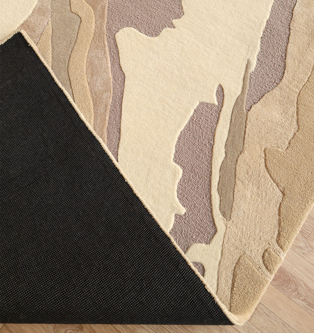 A close-up of the RAMSHA HOME Abstract Wool & Viscose Handmade Carpet 200x300 (HTWV-179), featuring layered cream, beige, brown, and taupe shapes with a textured black triangle on a light wood floor.