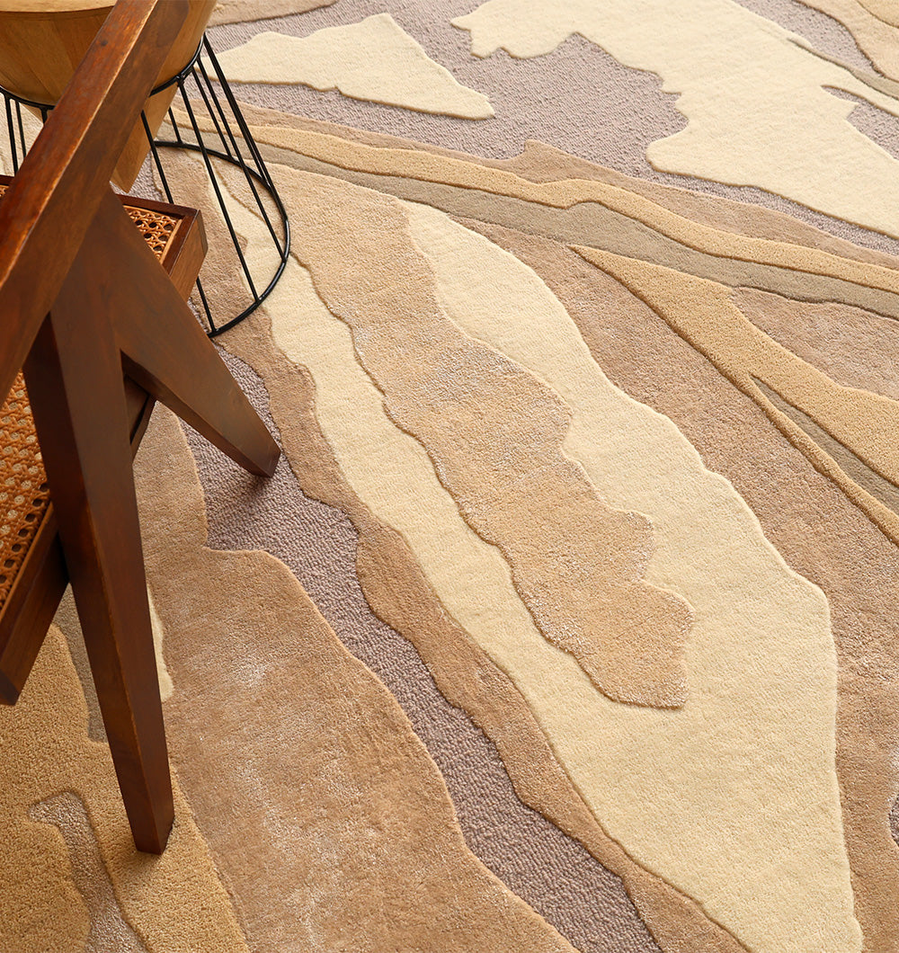 The RAMSHA HOME Abstract Wool & Viscose Handmade Carpet 200x300 – HTWV-179 in layered beige and tan tones is placed beneath a wooden chair with a woven seat and a round table featuring black metal legs.