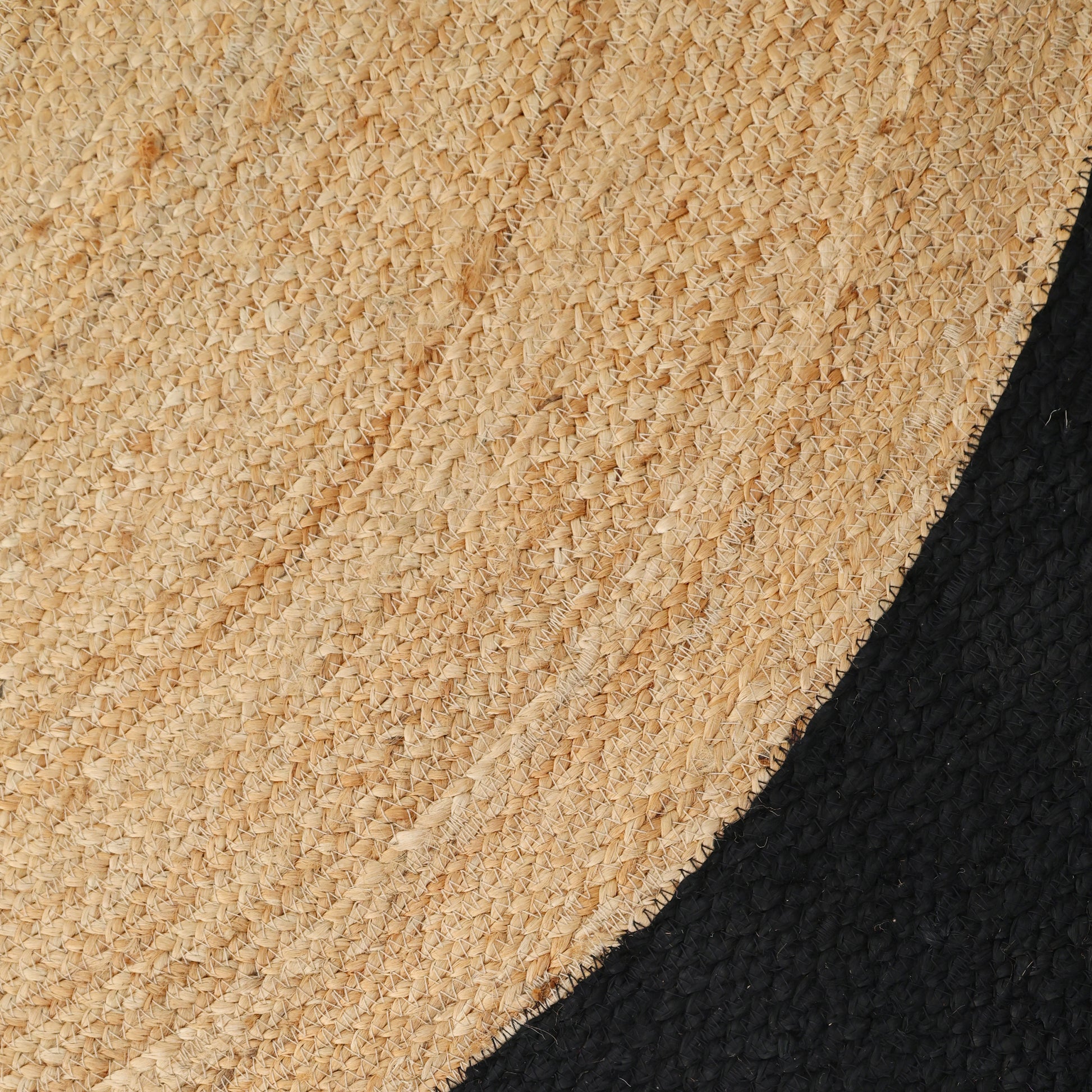 A close-up of the RAMSHA HOME Braided Rug Jute carpet for Bedroom Living Room Area Rug BR-003 shows its natural fibers and spiral pattern, partially covering a textured black surface.