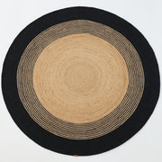 The RAMSHA HOME Luxurious Handmade Braided Jute Round Rug - BR 028 features a natural tan center, concentric black and tan stripes, and a solid black border—bringing timeless style to any space.