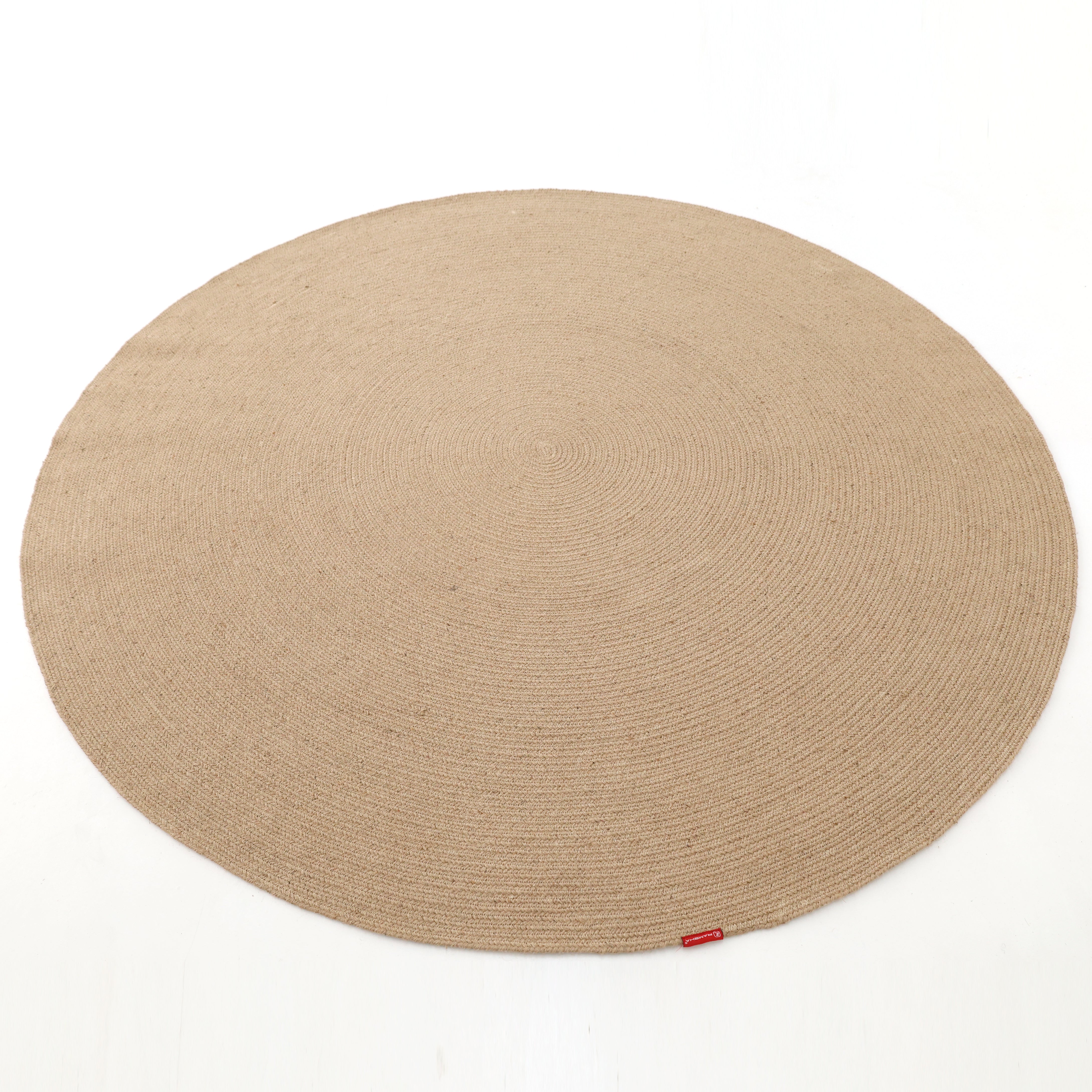 The RAMSHA HOME Stunning Handmade Jute Indoor & Outdoor Round Braided Rug - BR 014 features a subtle spiral pattern in beige, woven from natural jute. A small red tag accents the edge, shown here on a white background.