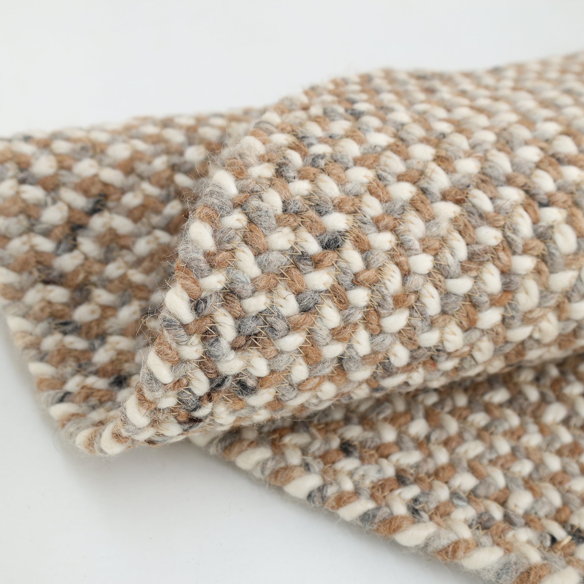 A close-up of the RAMSHA HOME Natural Color Dining Room Jute Area Braided Rug - BR 096, neatly folded to show its thick, chunky weave and stylish beige, brown, cream, and gray tones.