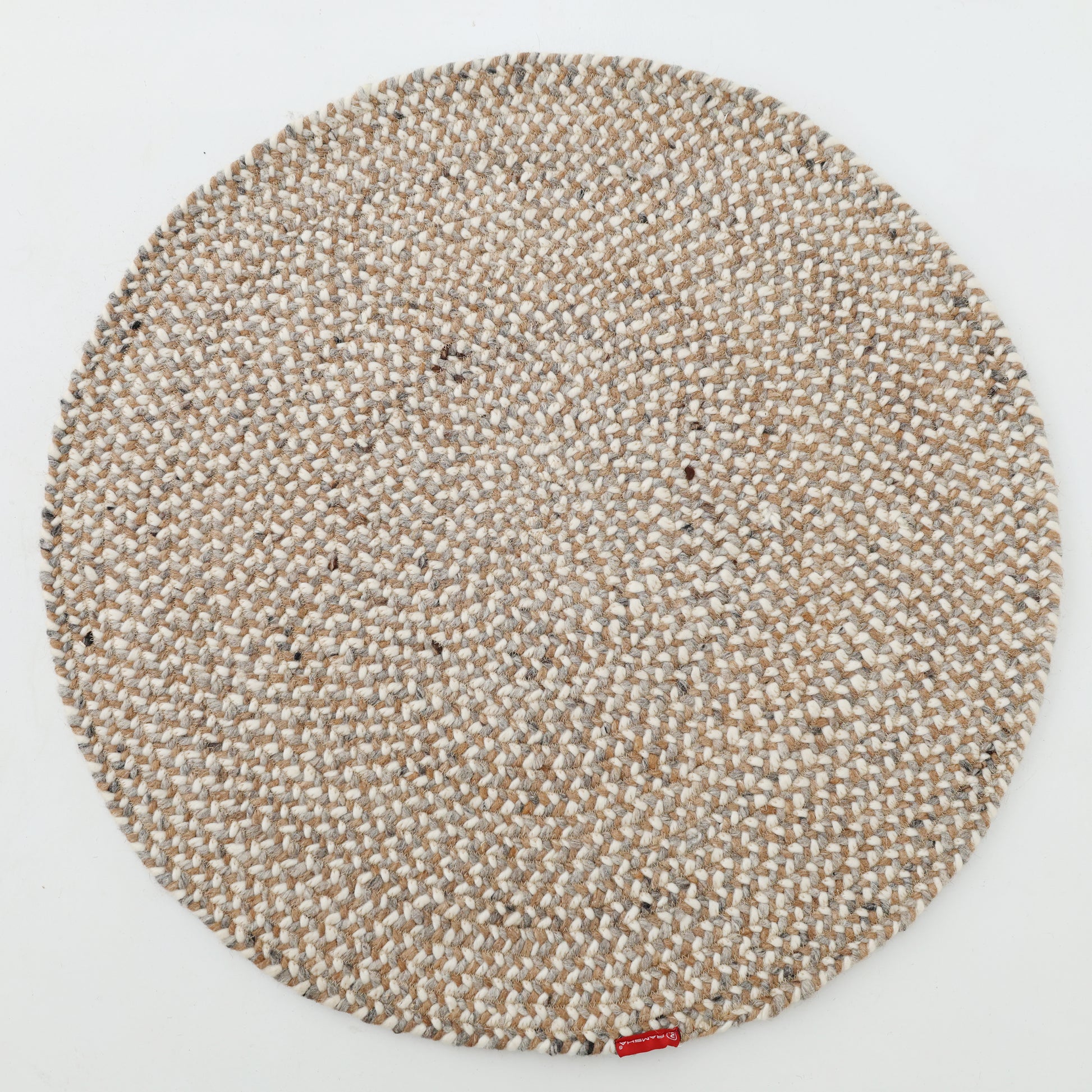 The RAMSHA HOME Natural Color Dining Room Jute Area Braided Rug - BR 096, a round beige and white rug with a braided texture, is shown on a white background with a small red label attached to its edge.