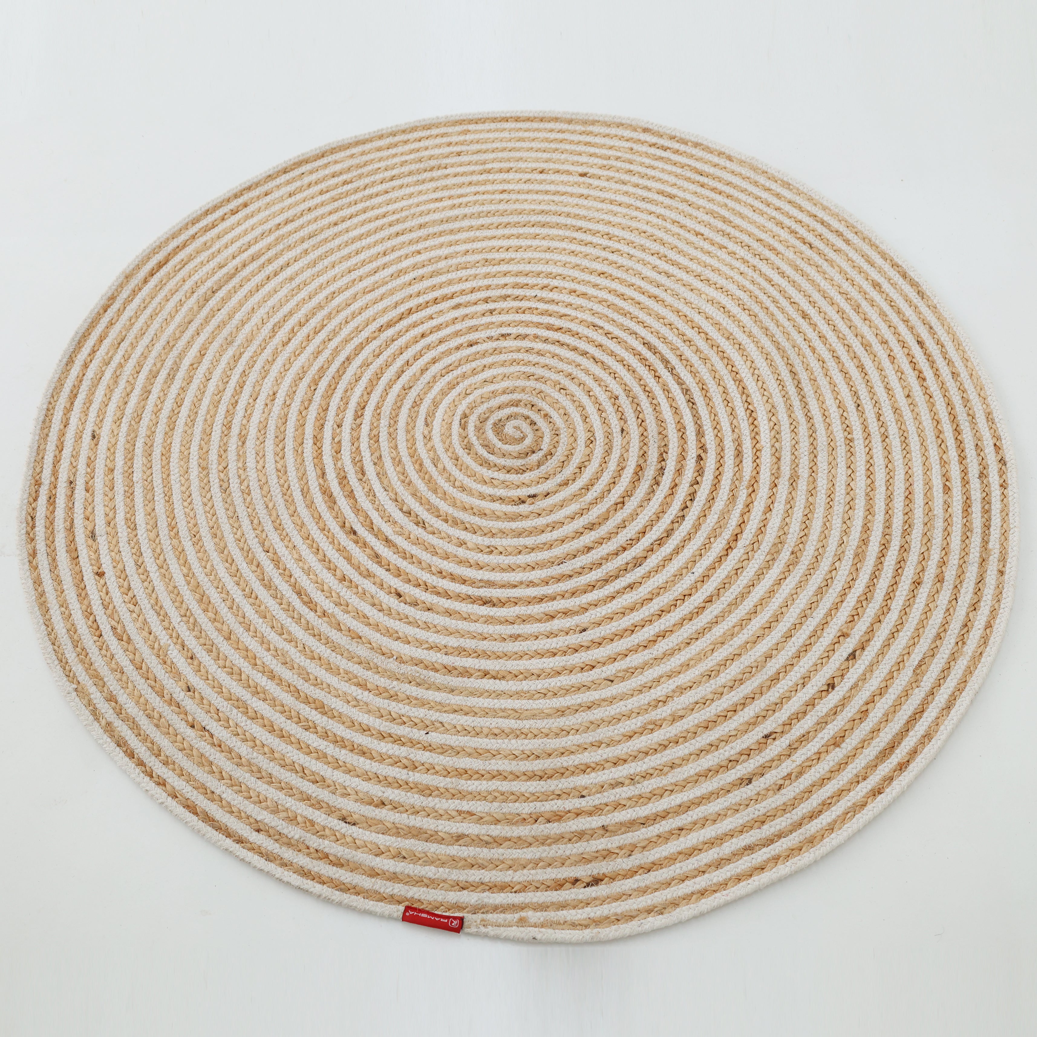 The Handmade Natural & White Color Braided Jute Round Rug - BR 012, featuring a spiral pattern in beige and off-white, is shown on a white background with a small red tag attached to its edge.