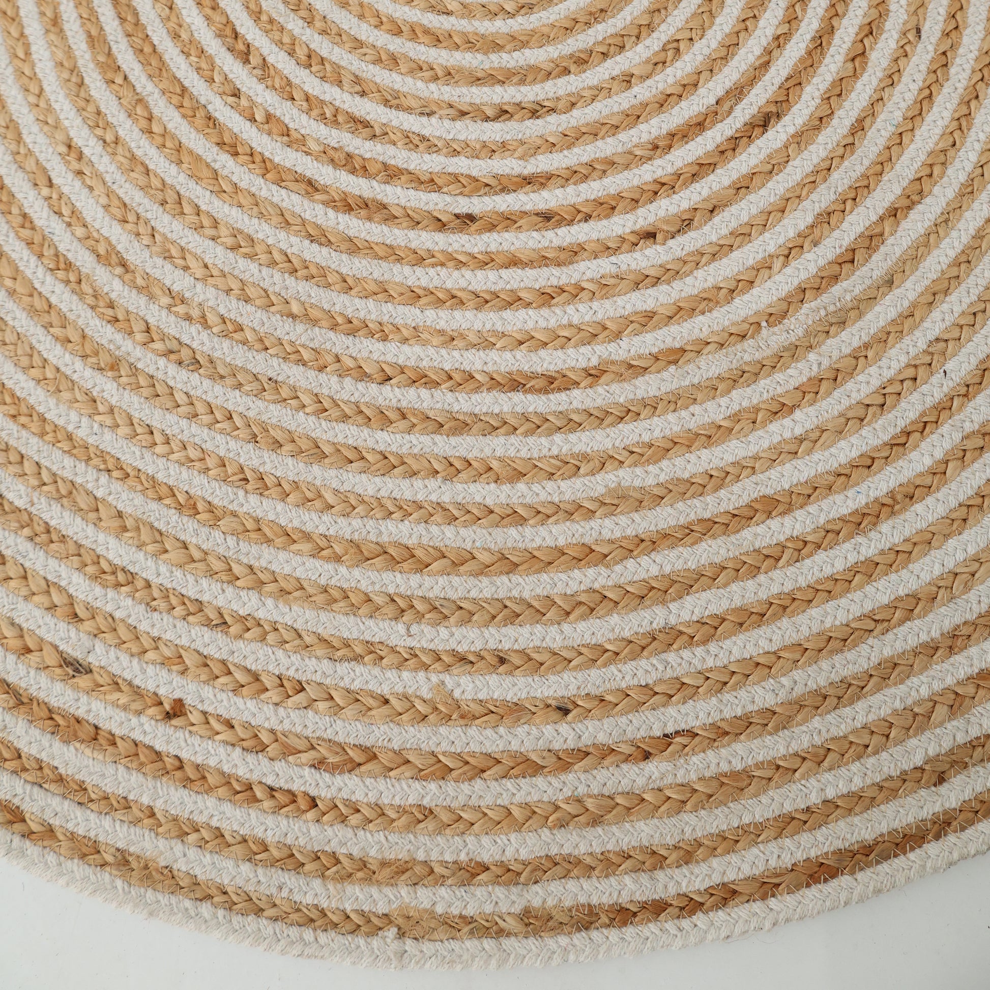 Close-up of the Handmade Natural & White Color Braided Jute Round Rug (BR 012), with alternating natural and white concentric circles forming a textured spiral pattern on a white background.