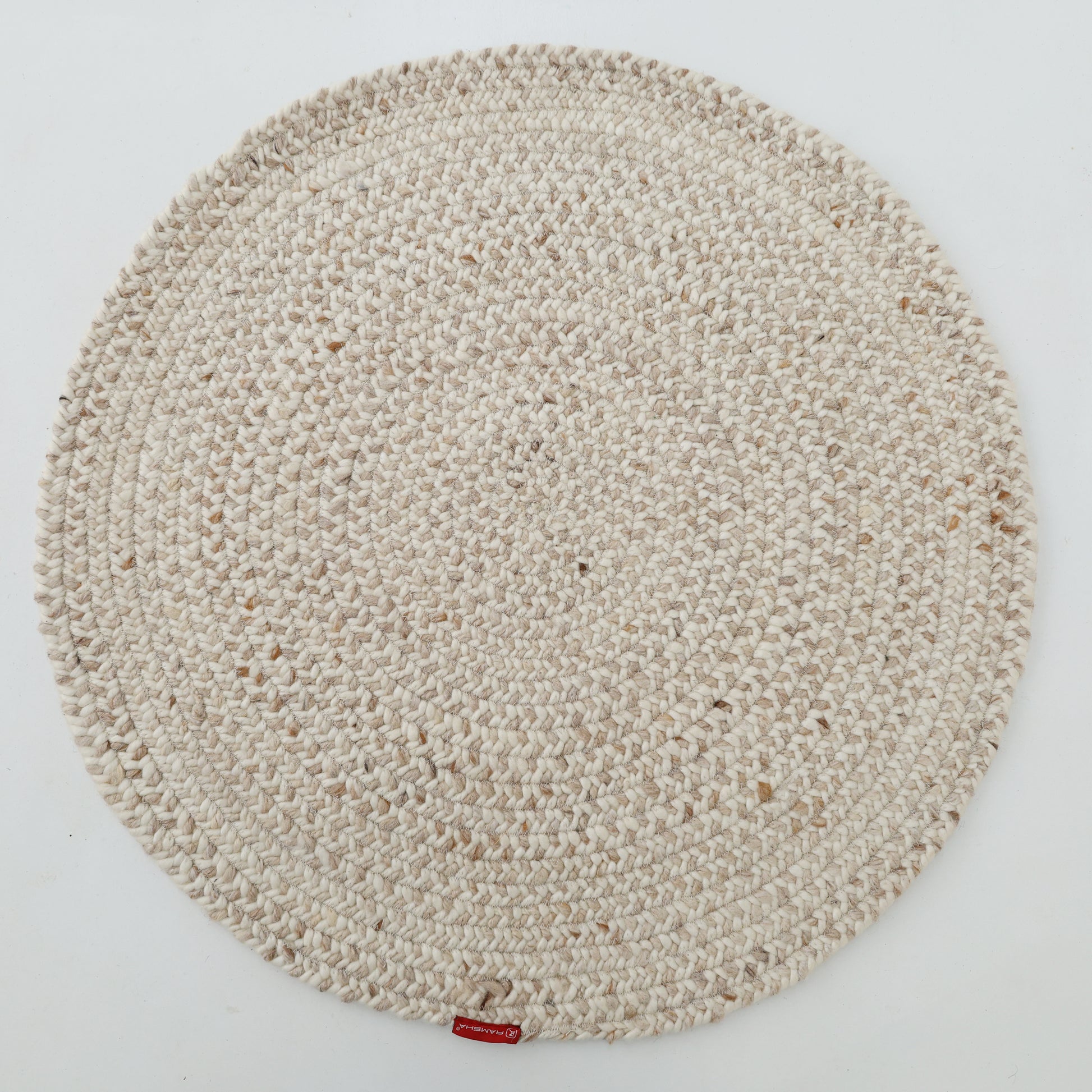 The RAMSHA HOME Natural Color Home Decor Round Jute Rug - BR 095 is a beige, textured rug with a small red tag on its edge, shown on a white background.